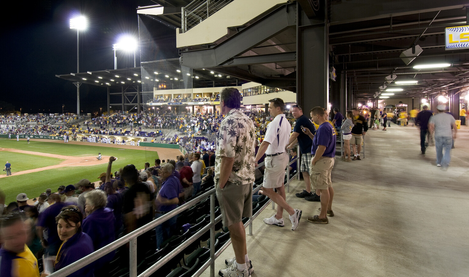 Covered walkway behind the top of lower deck seating behind home plate with box suites overhead supported by exposed beams