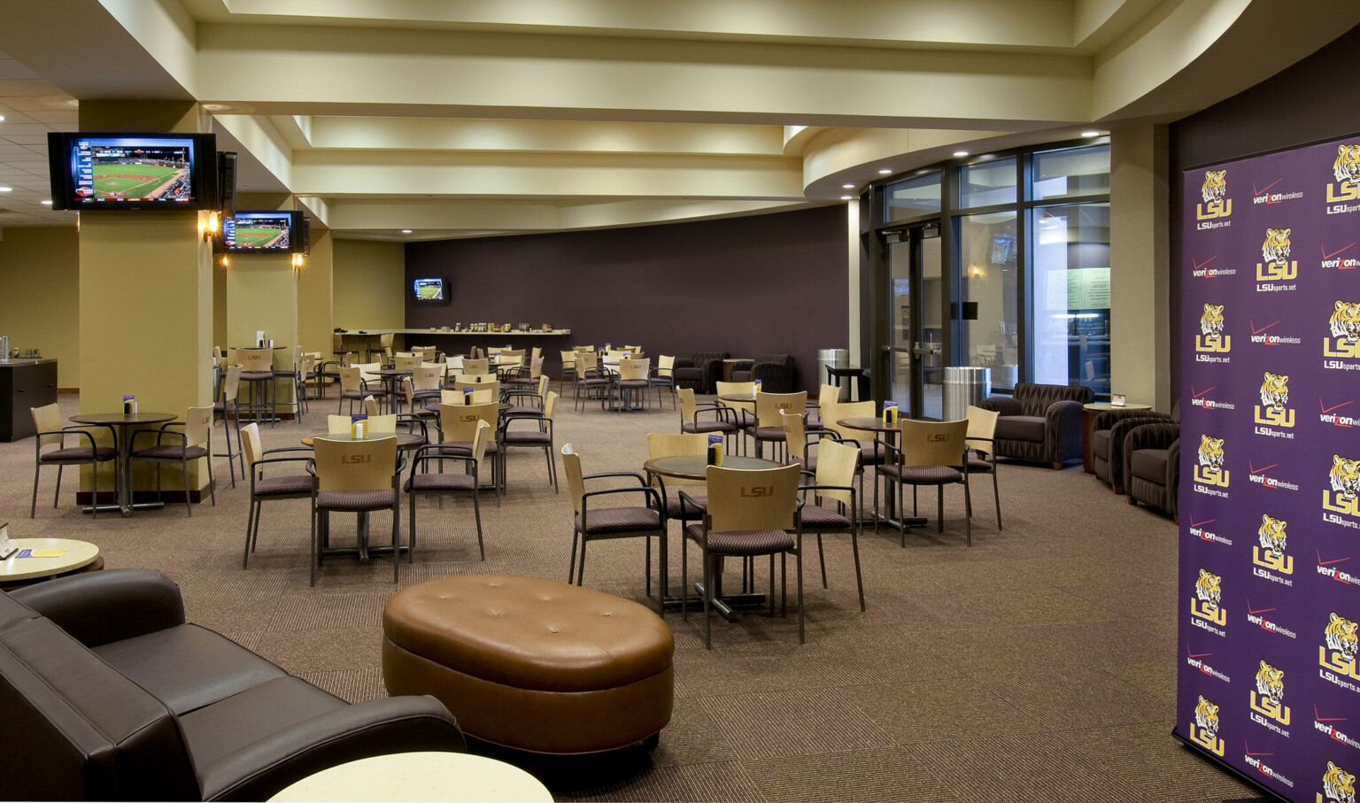 Dining area with rounded glass entry. LSU logo on chair backs in cream room. Screens on columns, purple accent wall right