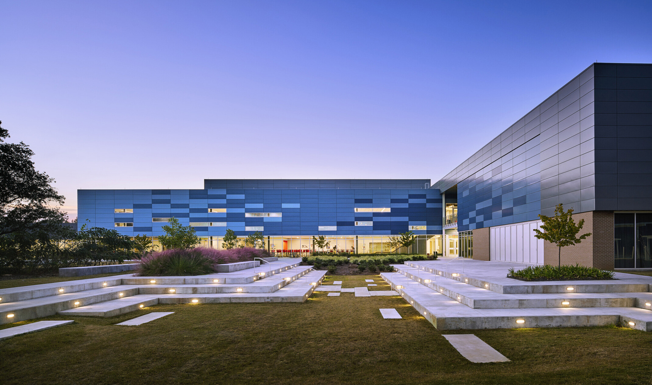 evening image of a modern building courtyard/ greenspace; modern white seats with small ground lights