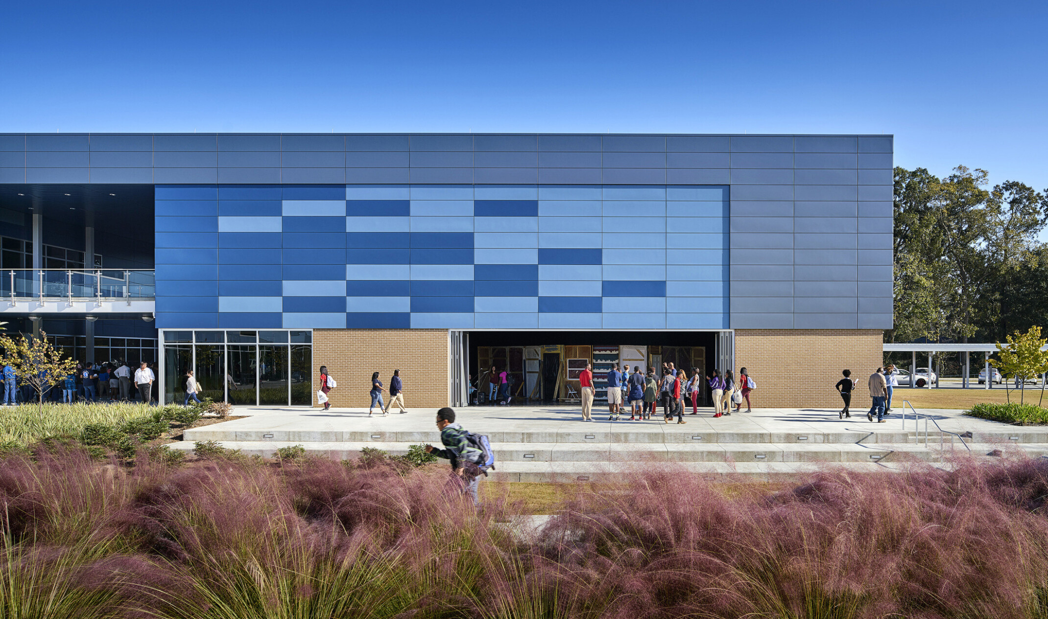 Front facade of a high school with lush native plants in the foreground against a modern school builidng