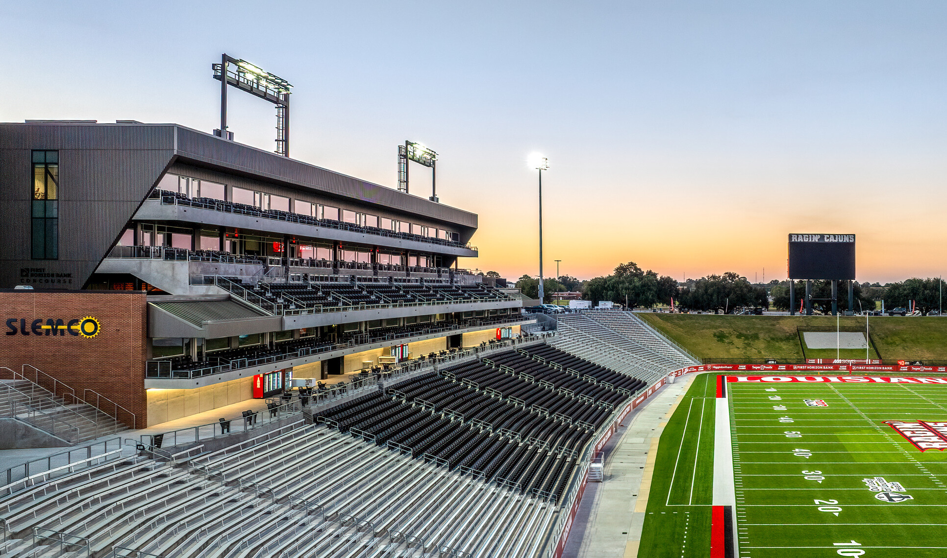 Modern football stadium with multi-level seating, suites, and a scoreboard, photographed at dusk from the stands overlooking the field.
