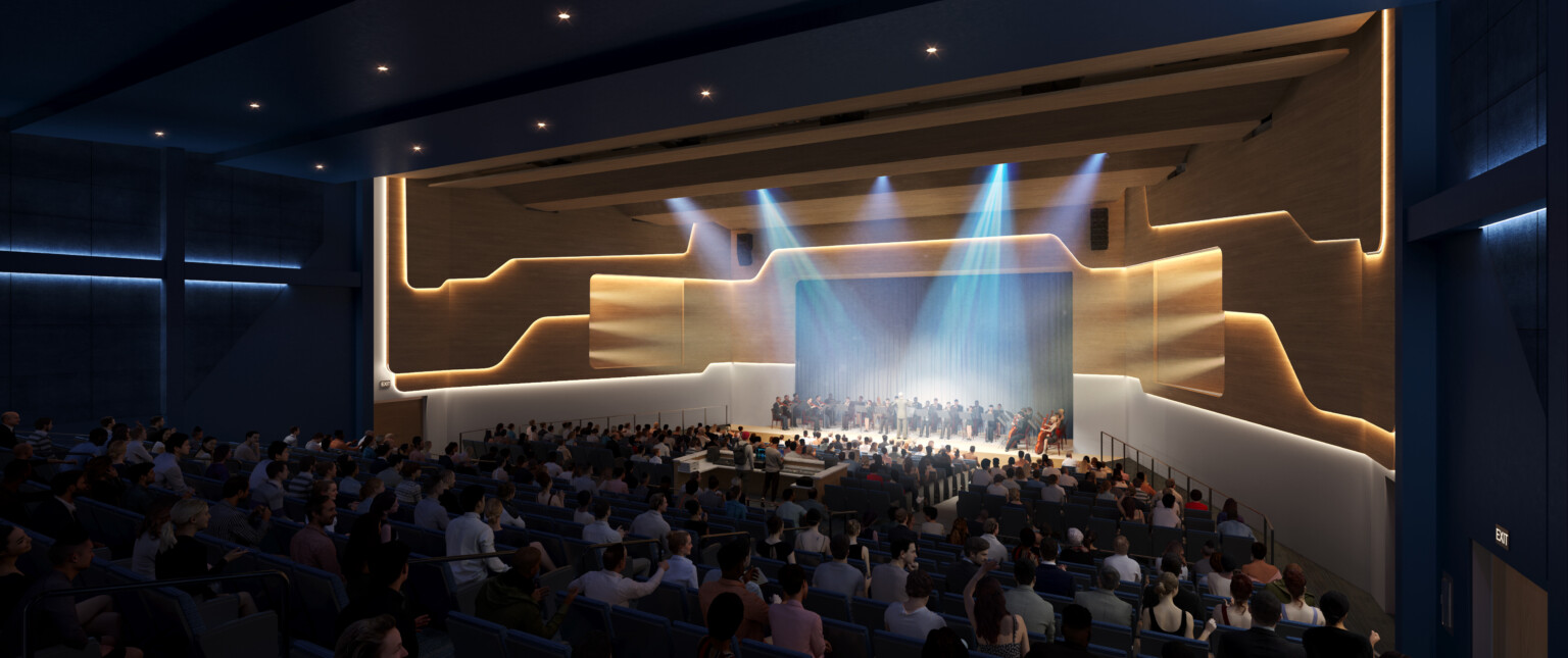 Dark high school auditorium with a stage light by spotlights filled with students