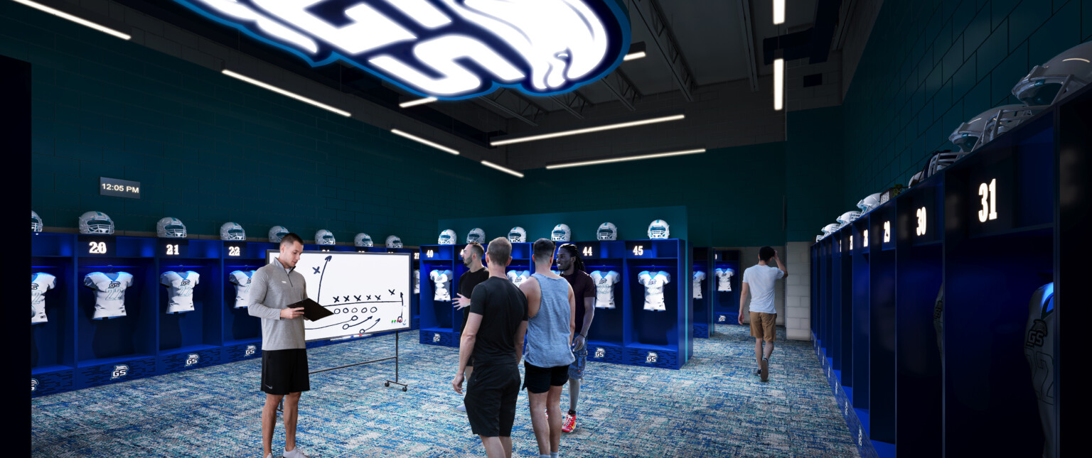 High school locker room filled with blue lockers with uniforms hanging inside and helmets on top with letters GS on the ceiling