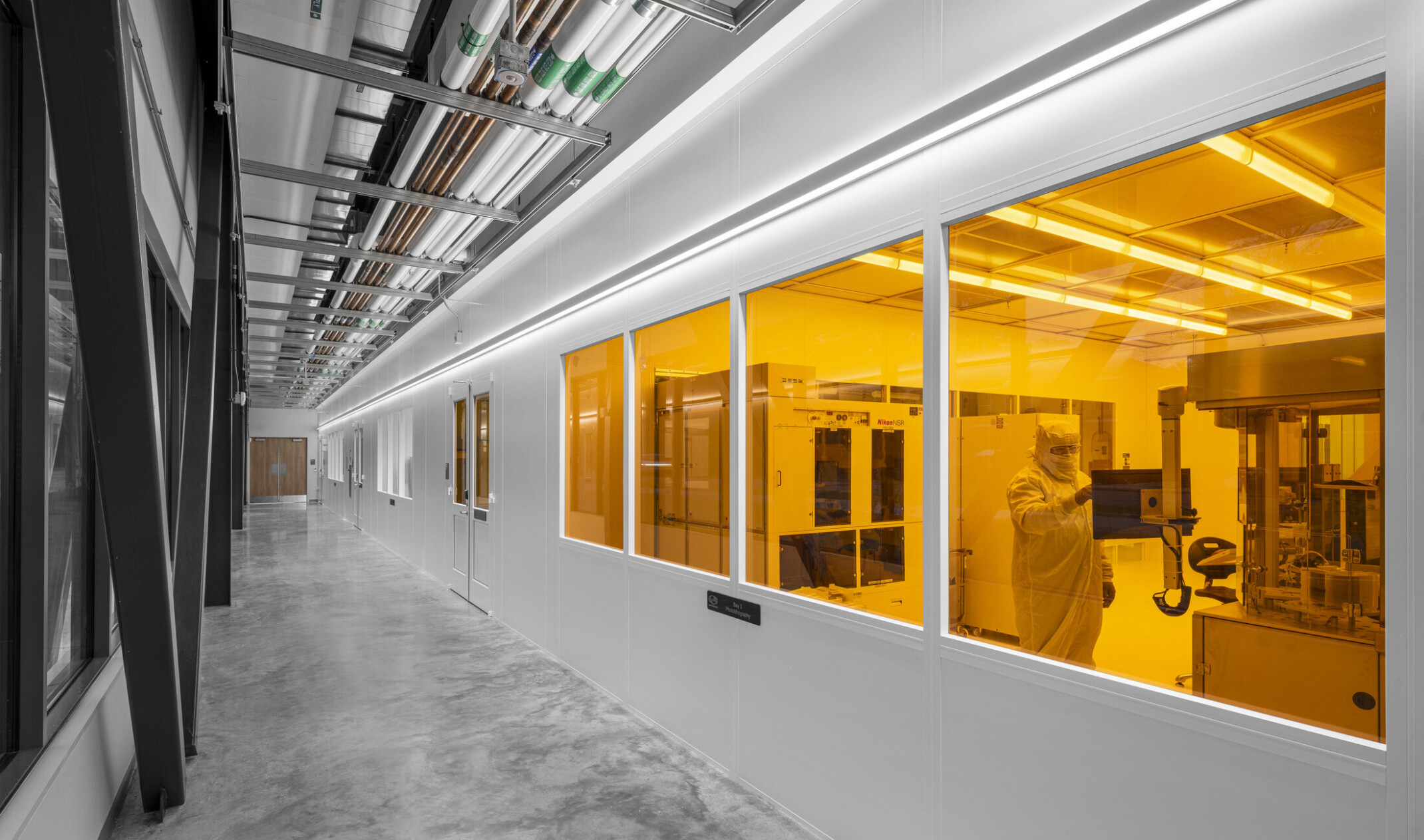 interior hallway of a lab facility with windows looking into an orange lit laboratory