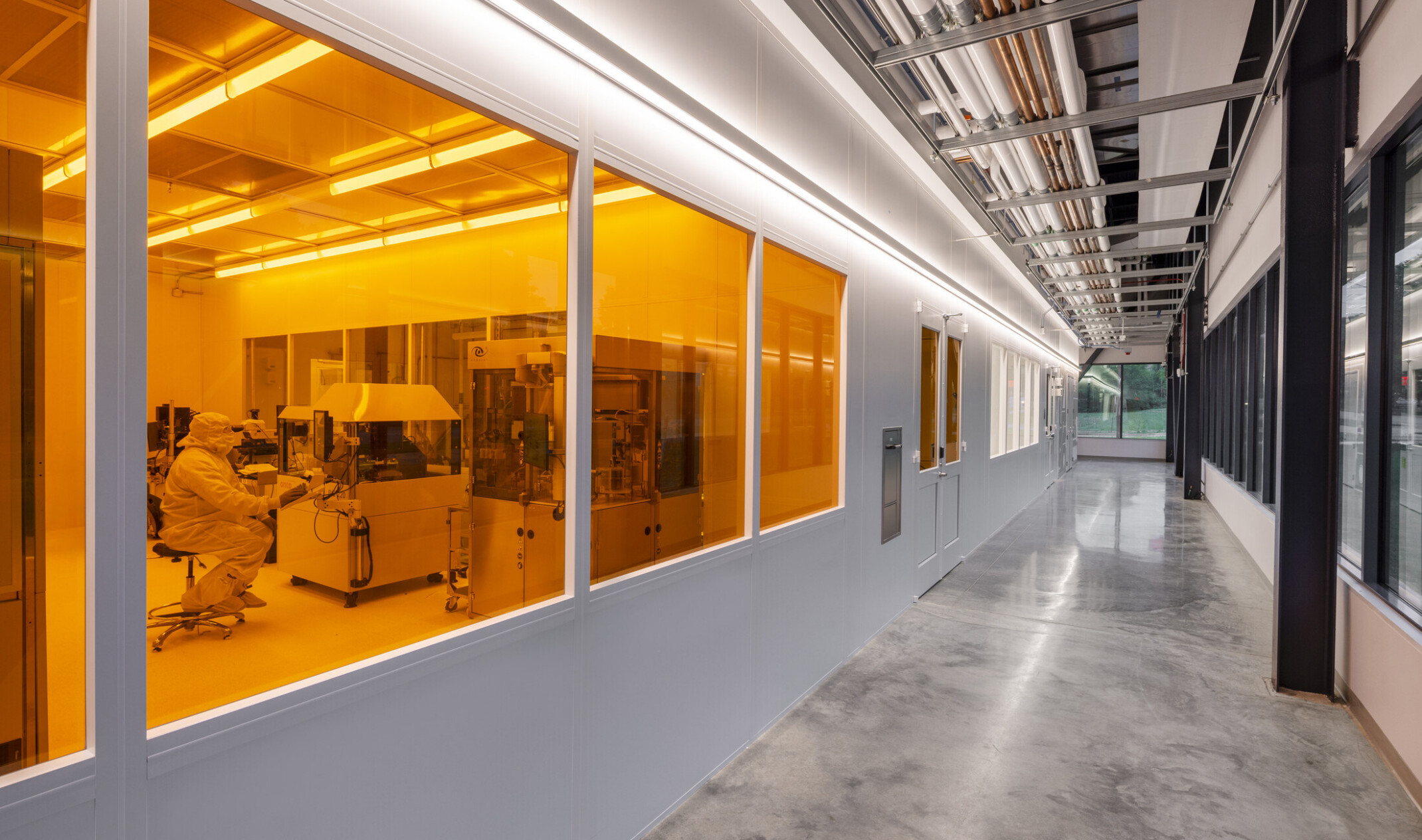 interior hallway of a lab facility with windows looking into an orange lit laboratory