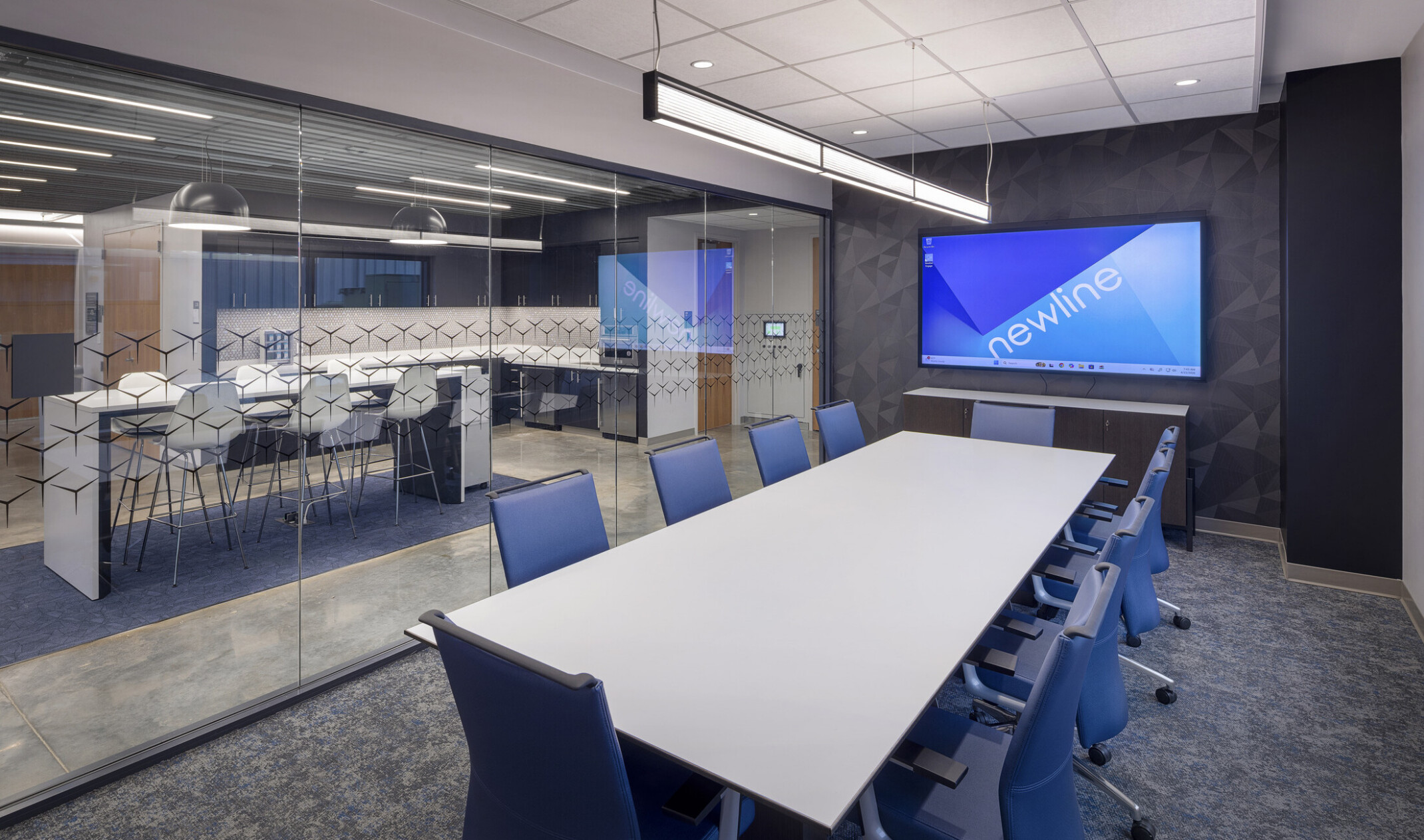 interior workplace conference room; long table with blue chairs faces a large TV screen