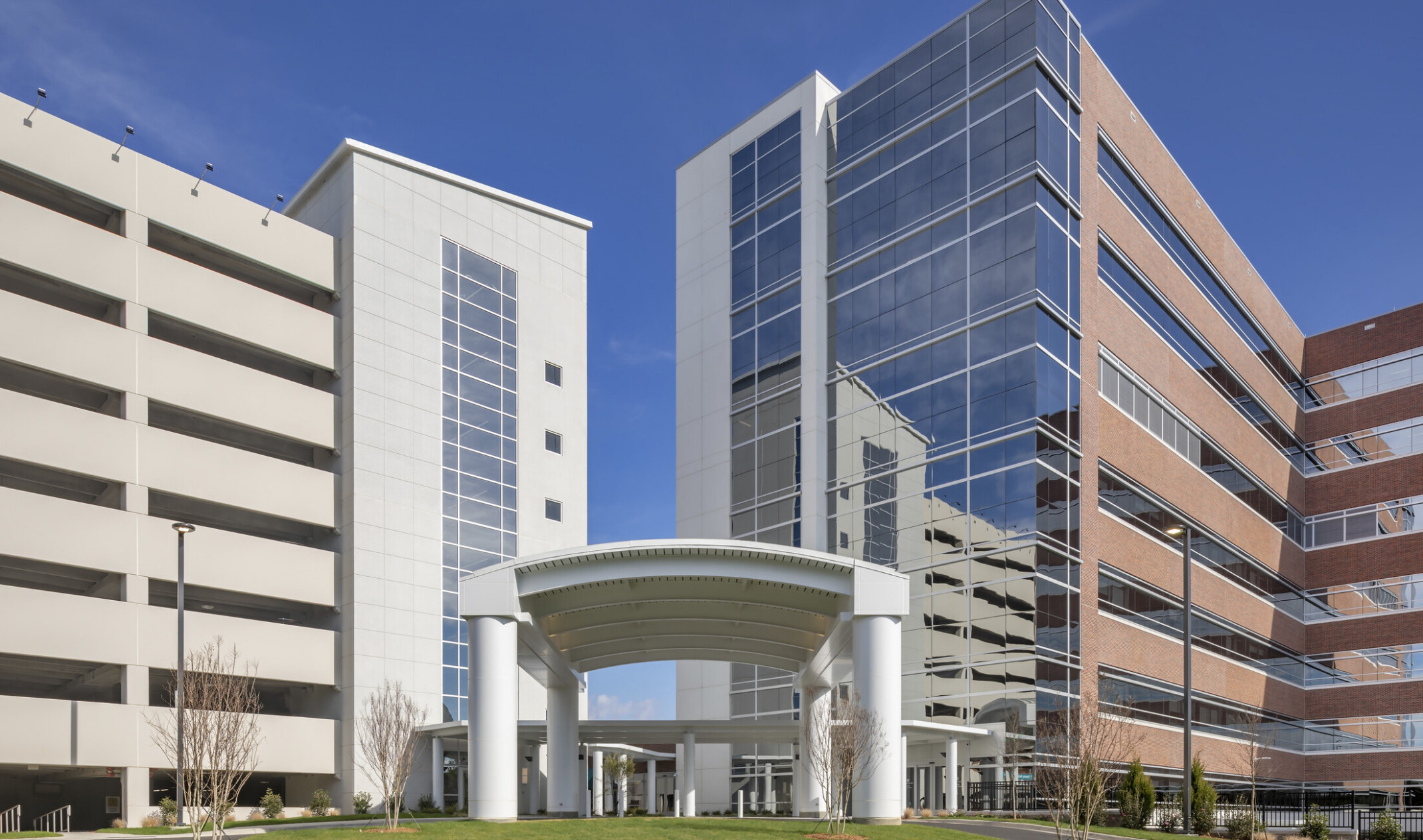 Atrium Health Pineville Bedtower Expansion. A multistory tower with white arching carport over drive. Garage to left
