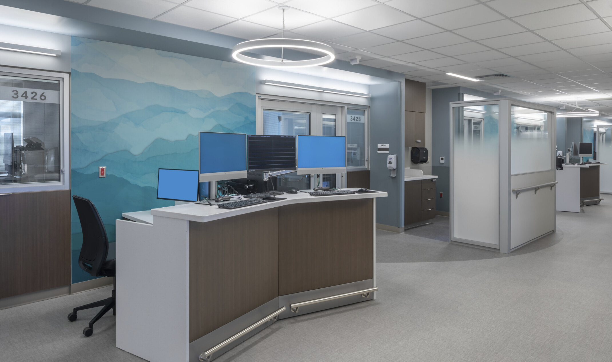 hospital nurse's desk area with computers and hand washing stations in front of a multi-blue wall print