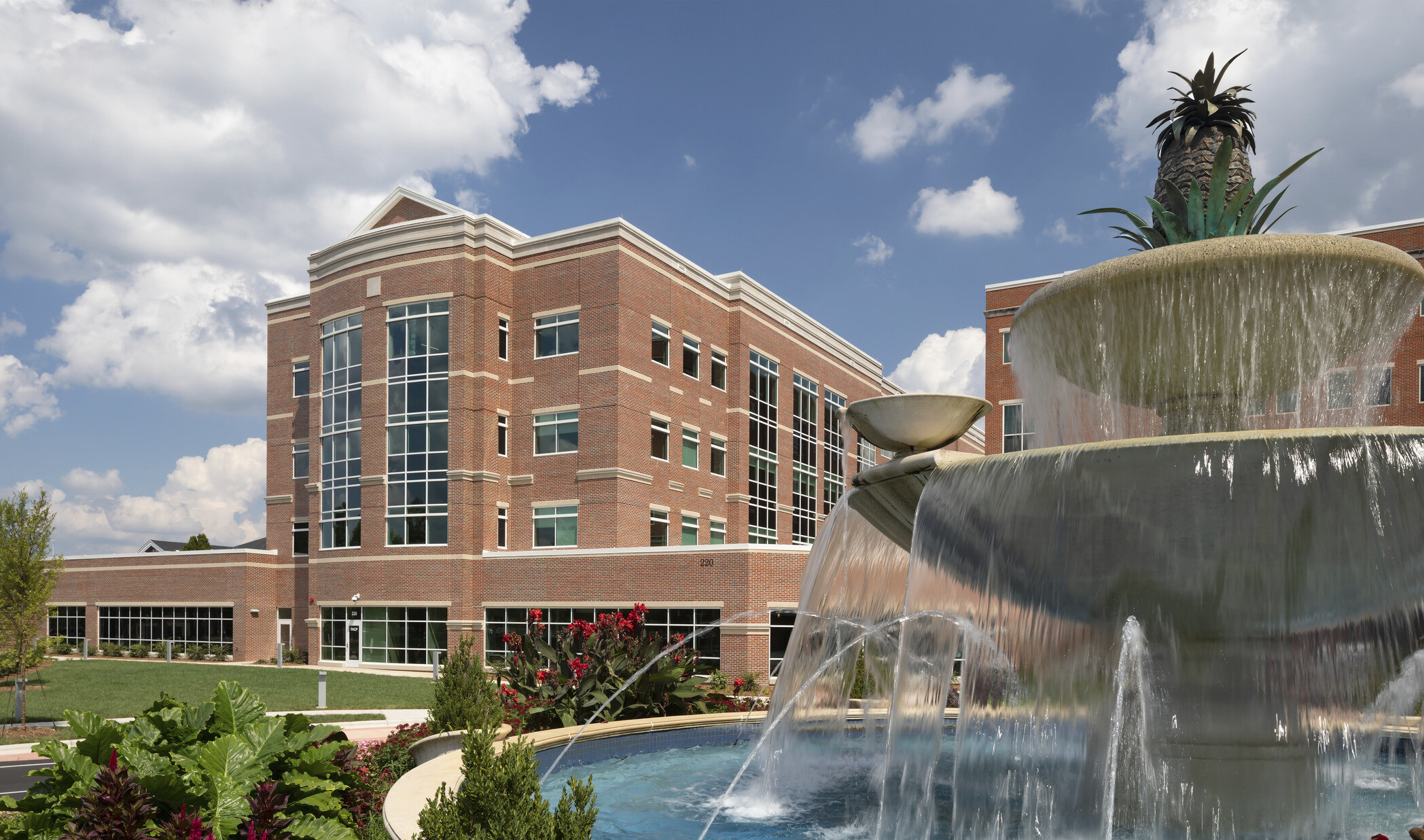 Atrium Health Cabarrus exterior, a brick building with windows along central tower. Landscaped grounds with stepped fountain