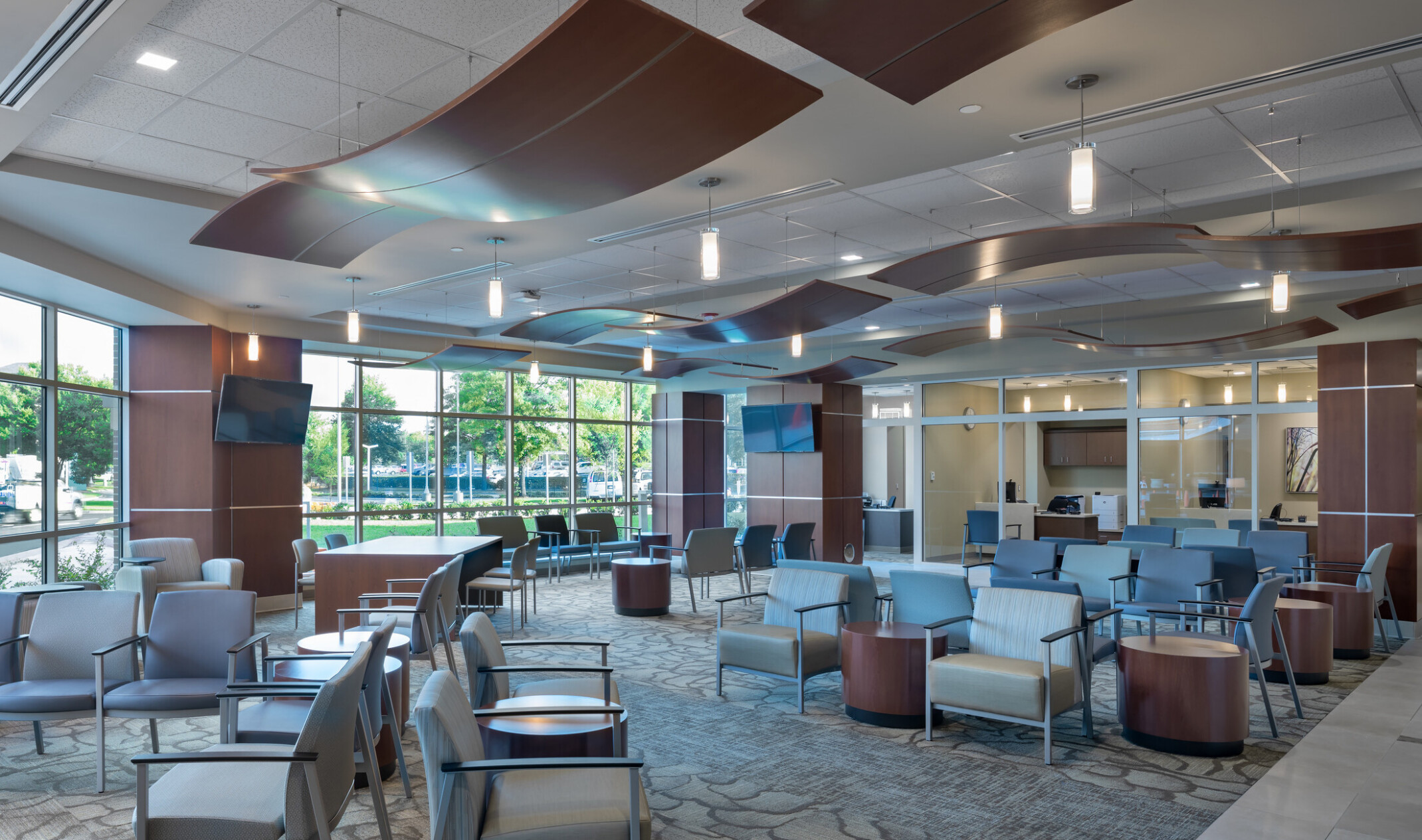 Waiting room lobby with flexible arm chairs and tables. Floor to ceiling windows to left, brown waving acoustic panels hanging