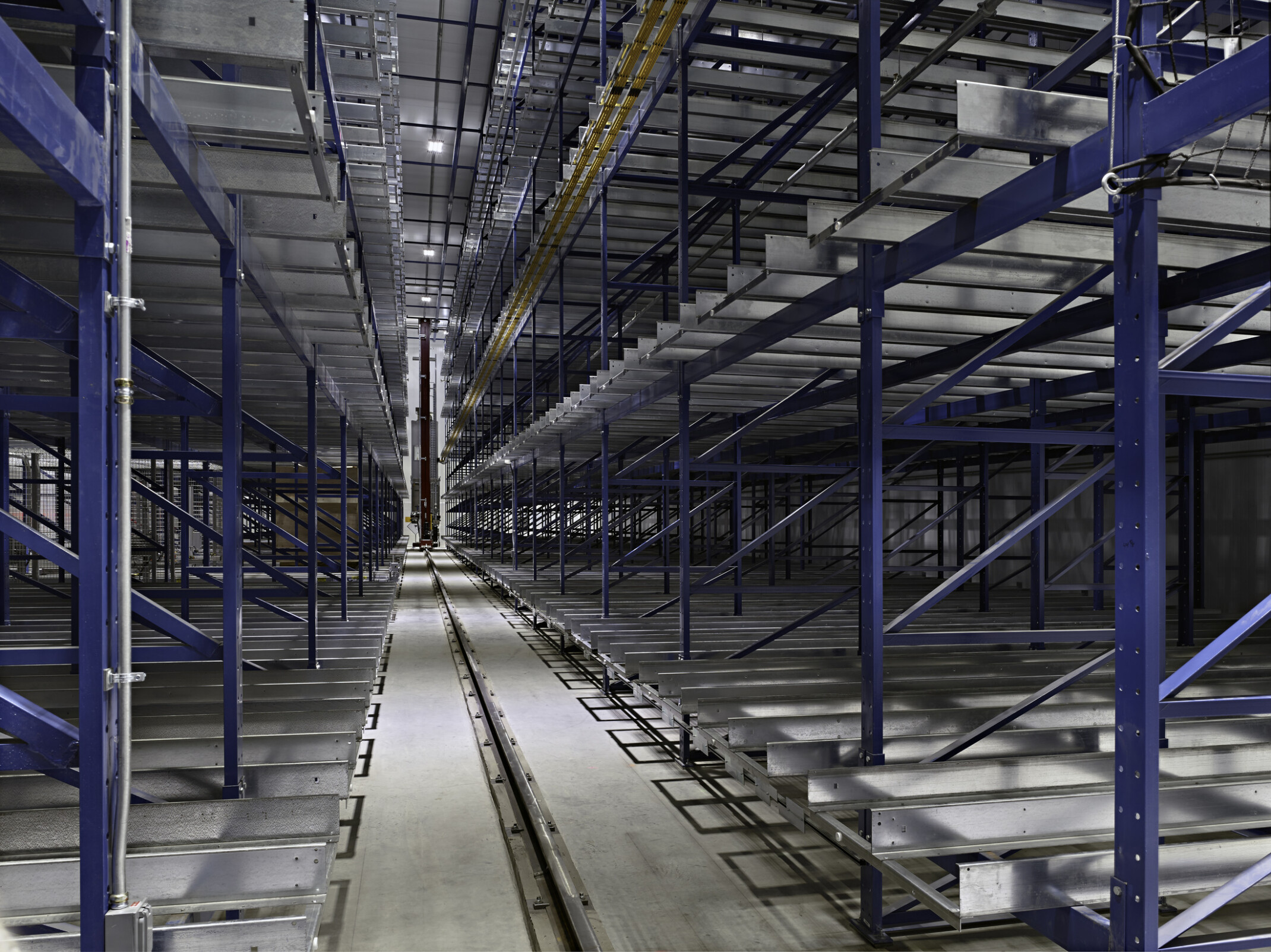 Interior view of Octapharma Plasma’s fully automated warehouse with empty storage racks and a robotic crane traveling along a central aisle track.
