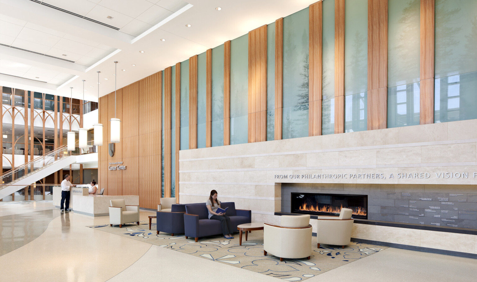 Front desk area of the Duke Medicine Cancer Center; light wood and blue accents on the wall offset the marble and tan desk and waiting area; lighting design and natural light make the space bright