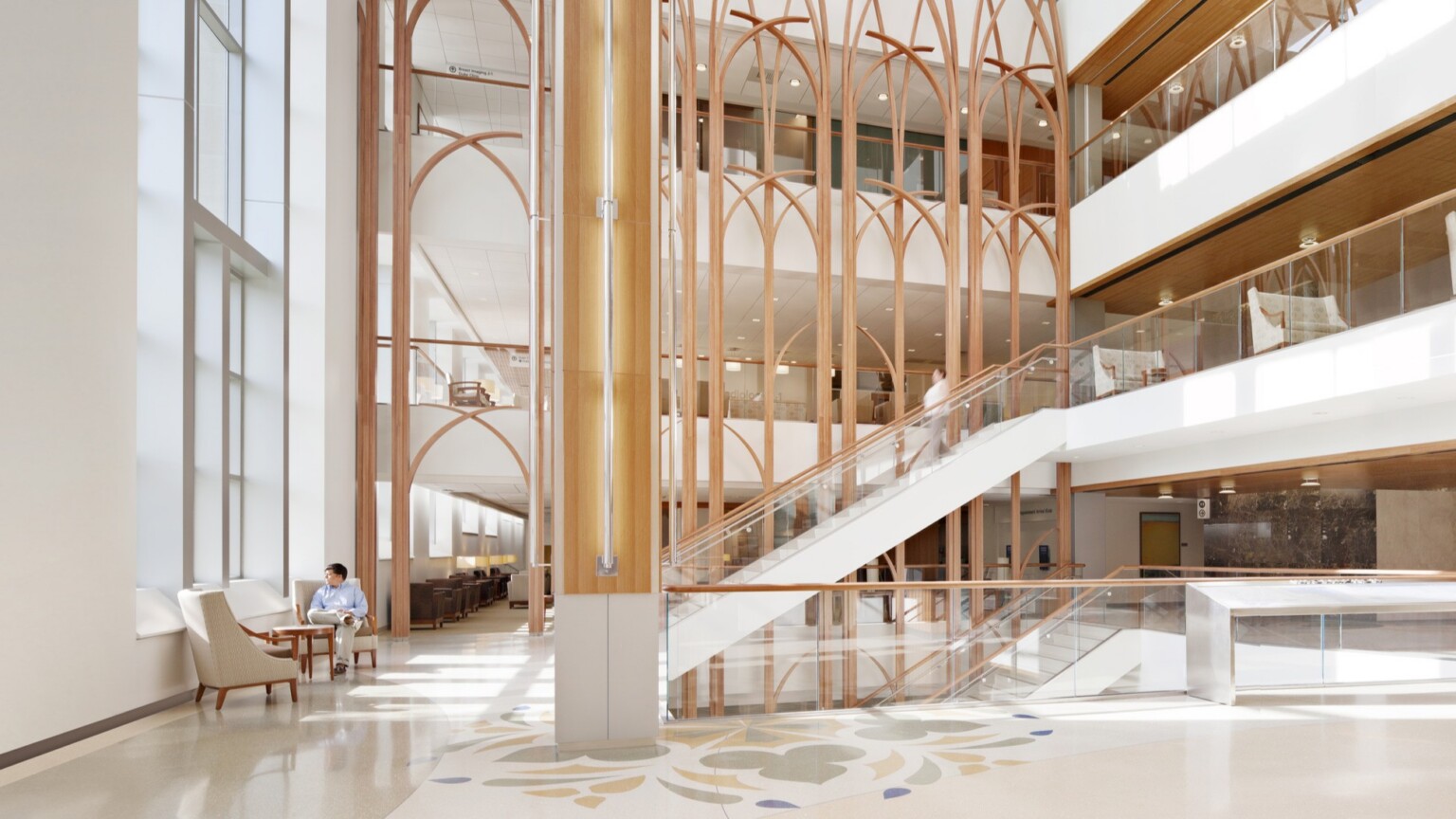 Large stairway area of the Duke Medicine Cancer Center; floor to ceiling windows light up the light wood design features in the large space; chairs and colorful floor detail decorate the space