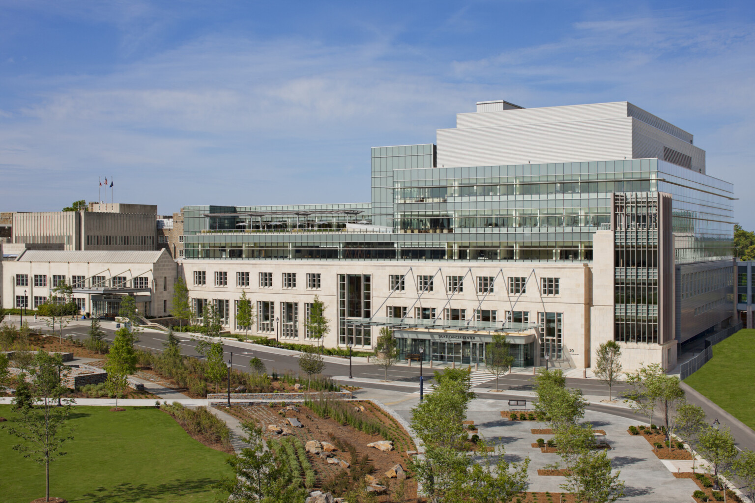Picture of the Duke Medicine Cancer Center; Large 7 floor building behind green walking space; floor to ceiling windows on the top floors of the building