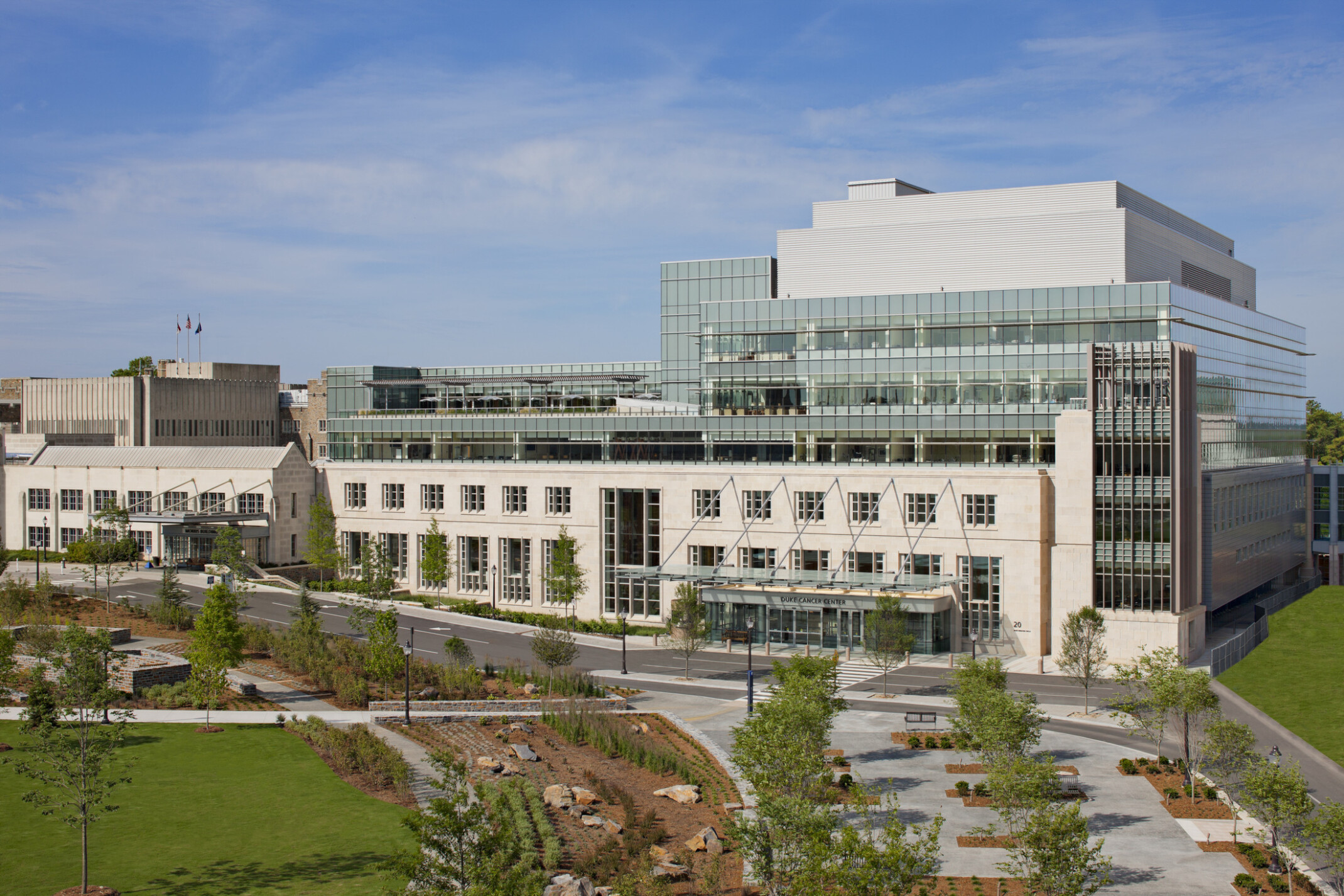 Picture of the Duke Medicine Cancer Center; Large 7 floor building behind green walking space; floor to ceiling windows on the top floors of the building