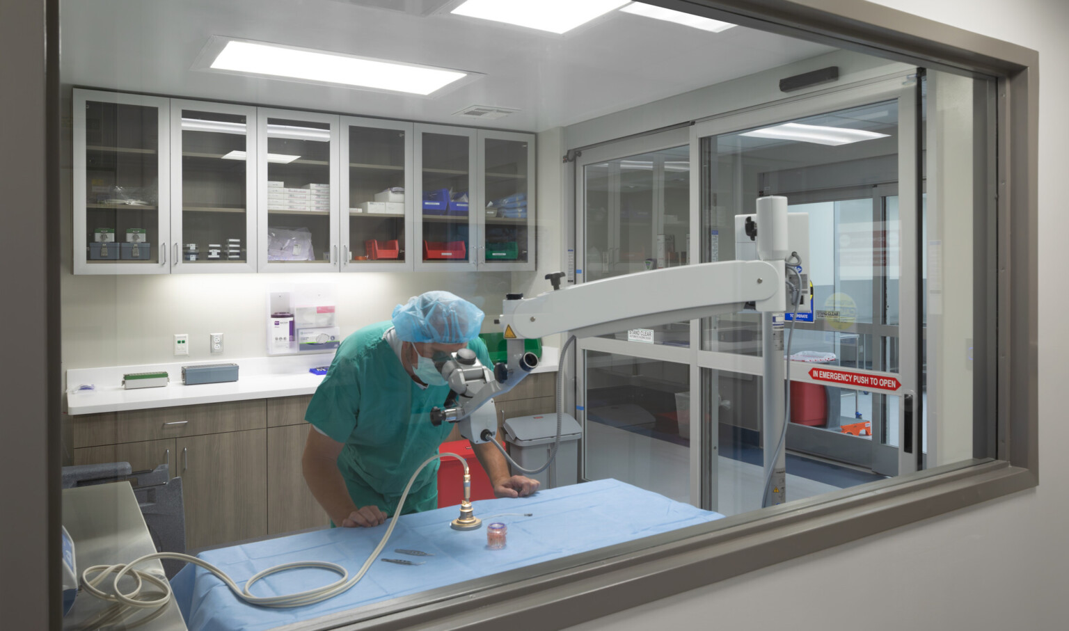 Hospital lab showing a technician in scrubs looking into a microsope
