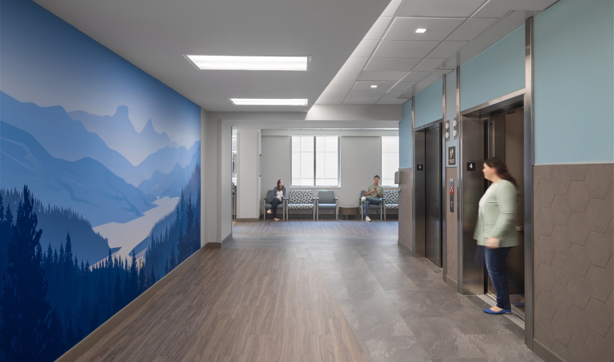Calming blue mountain mural faces the elevator bank with waiting room seats in the background