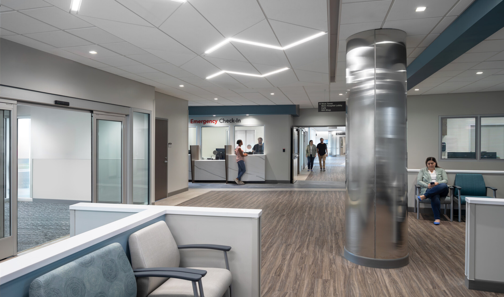 Waiting room at UNC Health Blue Ridge's New Healthcare Pavilion; blue and white seats in the forefront with a reception desk in the back left corner; large shiny mirror like column in the middle of the room