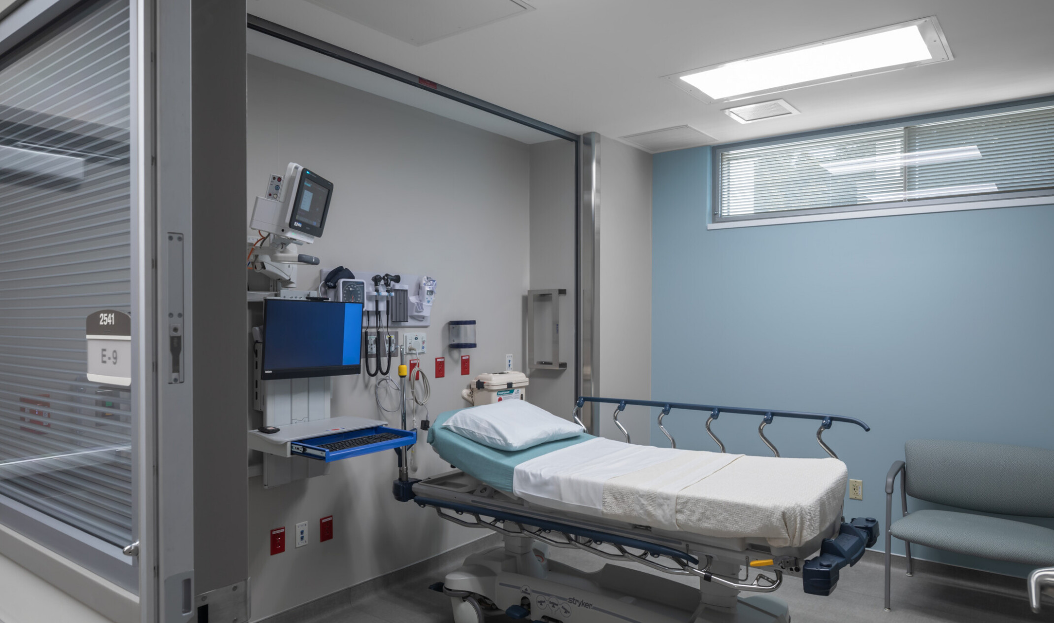 Modern hospital room with a bed, medical equipment, and a seating area by the bed