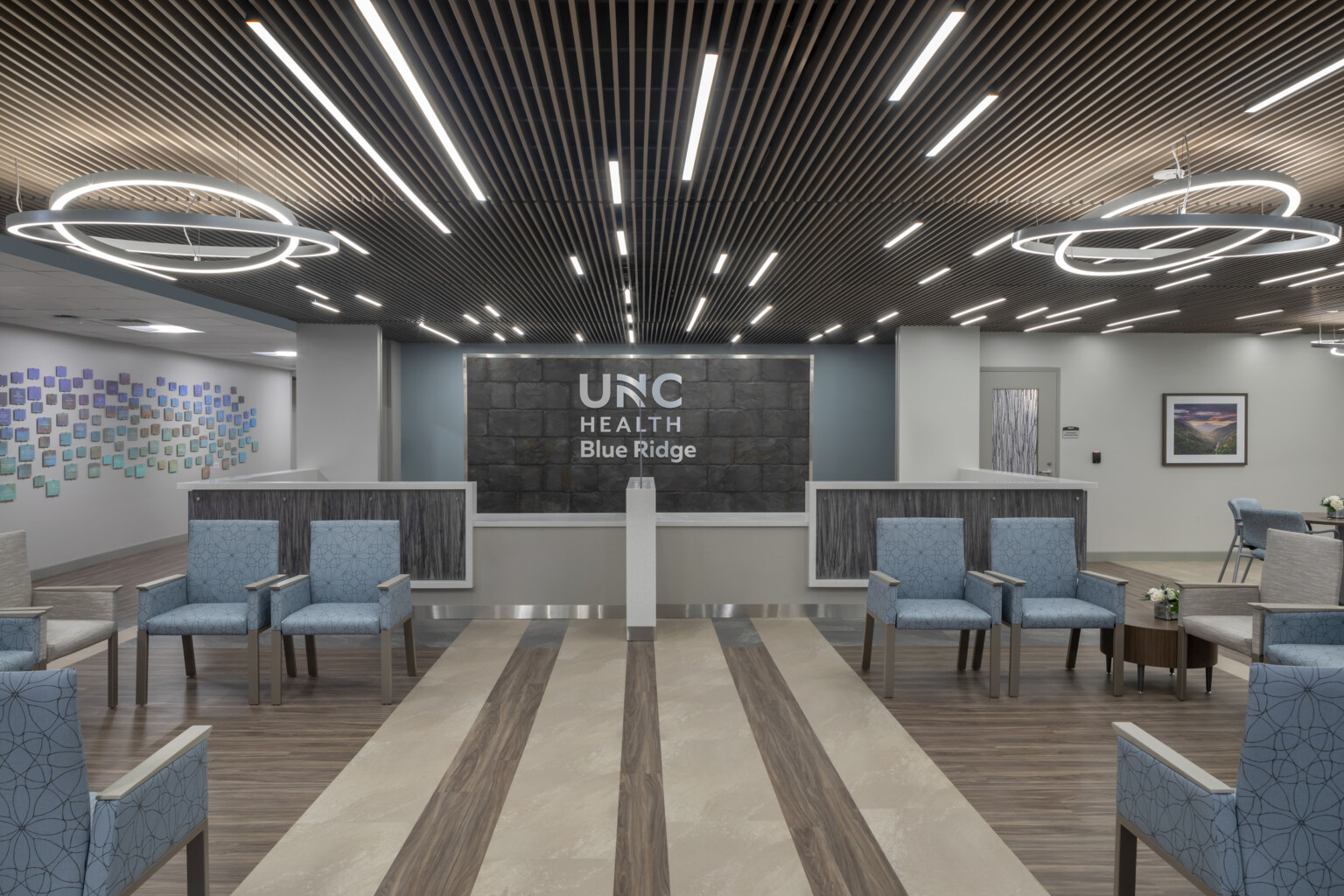 Medical waiting room filled with blue chairs, modern circular lighting hanging from the ceiling, and UNC Health Blue Ridge on the back wall