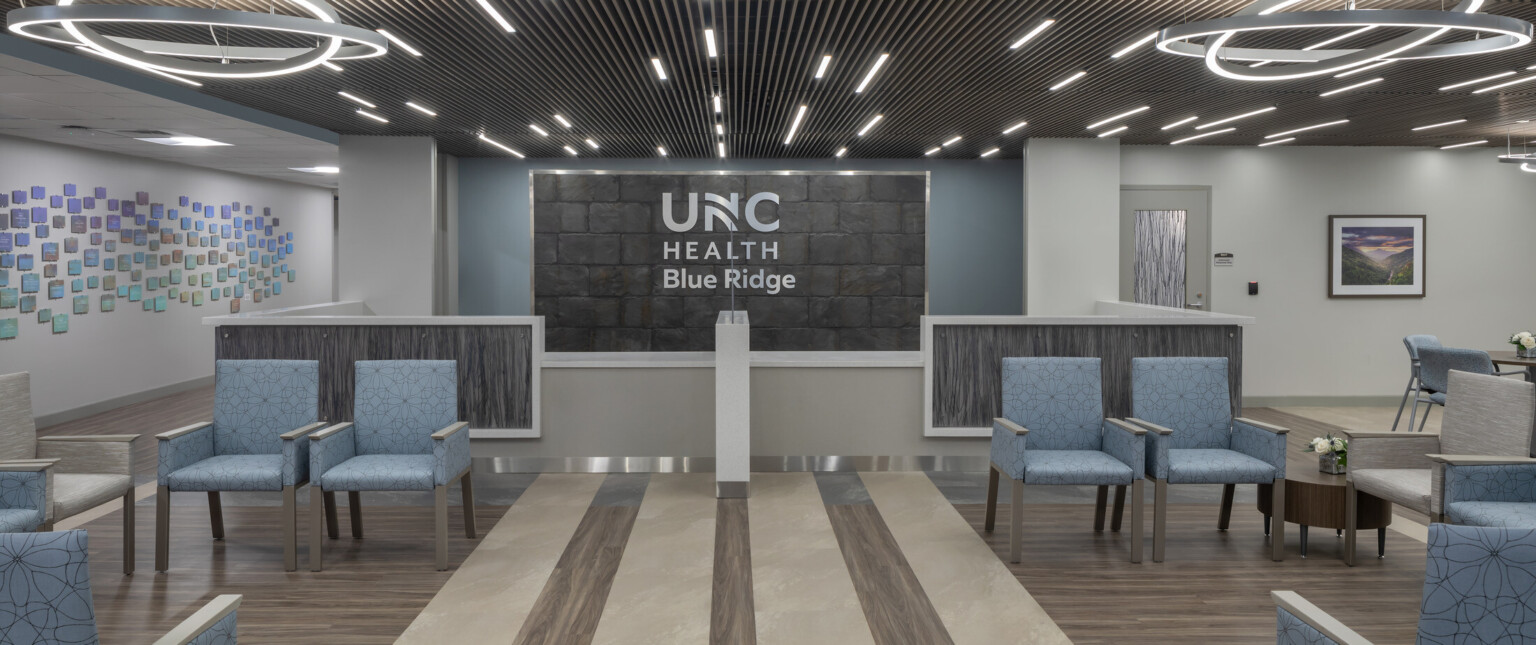 Medical waiting room filled with blue chairs, modern circular lighting hanging from the ceiling, and UNC Health Blue Ridge on the back wall