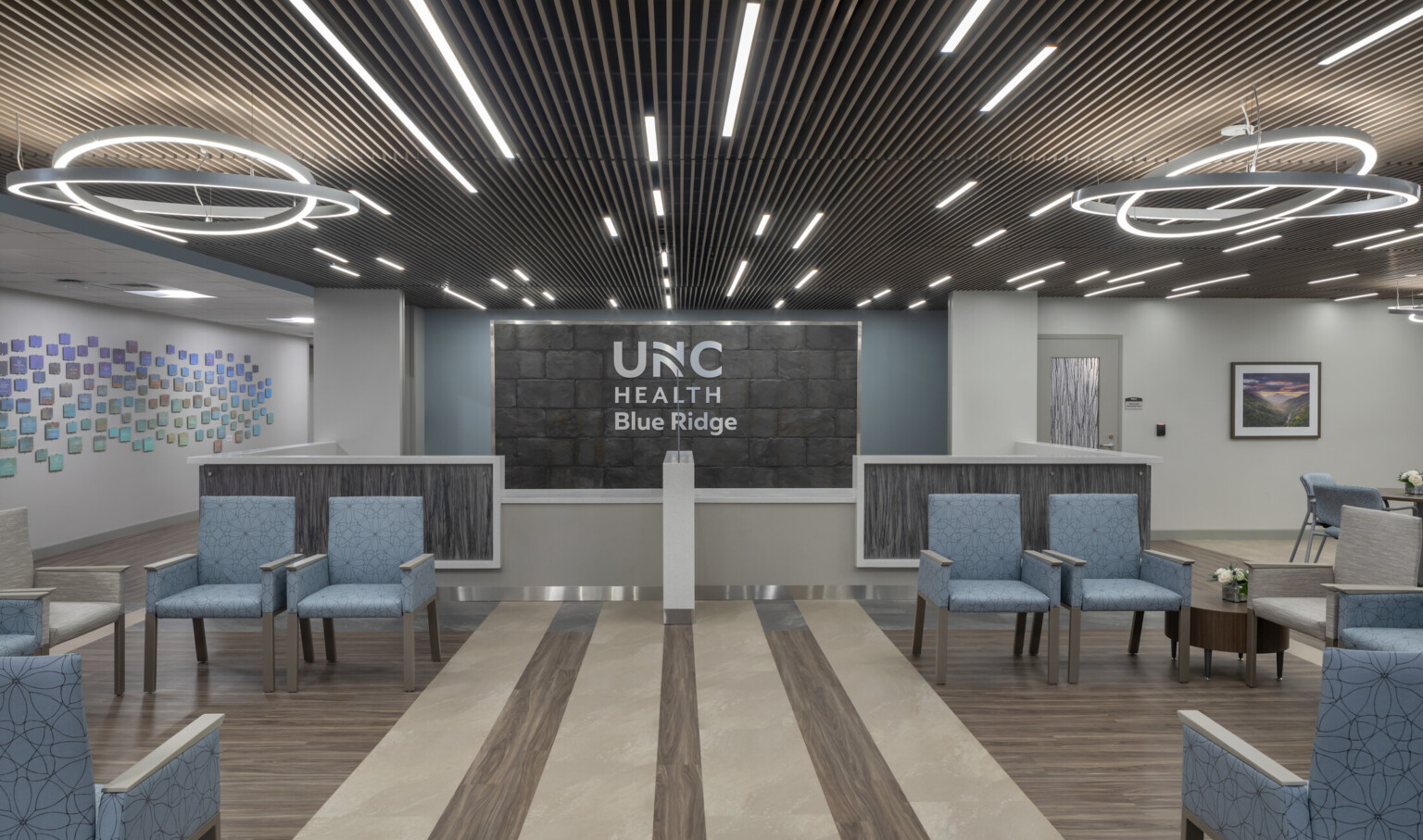 Medical waiting room filled with blue chairs, modern circular lighting hanging from the ceiling, and UNC Health Blue Ridge on the back wall
