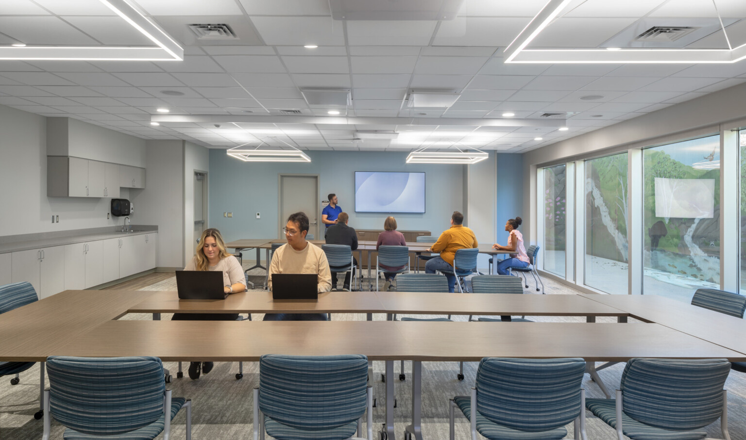 Classroom filled with students sitting at rectangular tables with modern square lights suspended from the ceiling