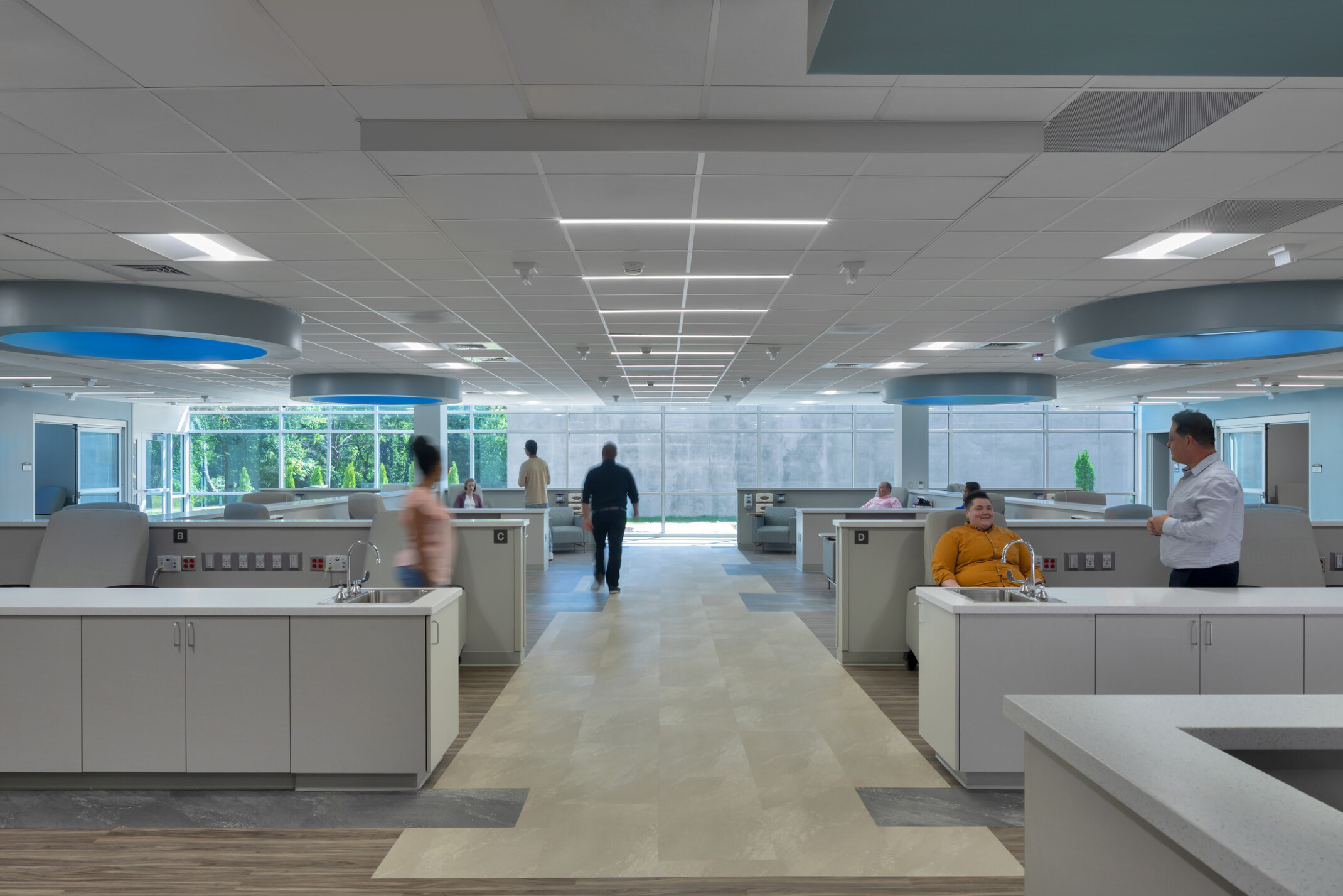 Infusion center showing patients waiting to be evaluated, courtyard seen in background through large windows