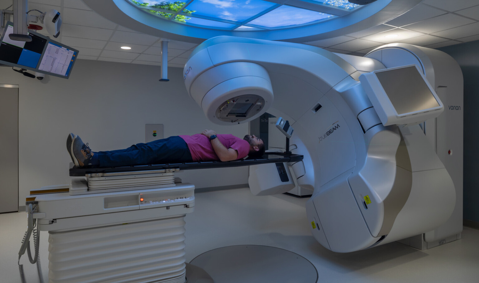 Person laying on a table being scanned by medical equipment with a large circular window overhead