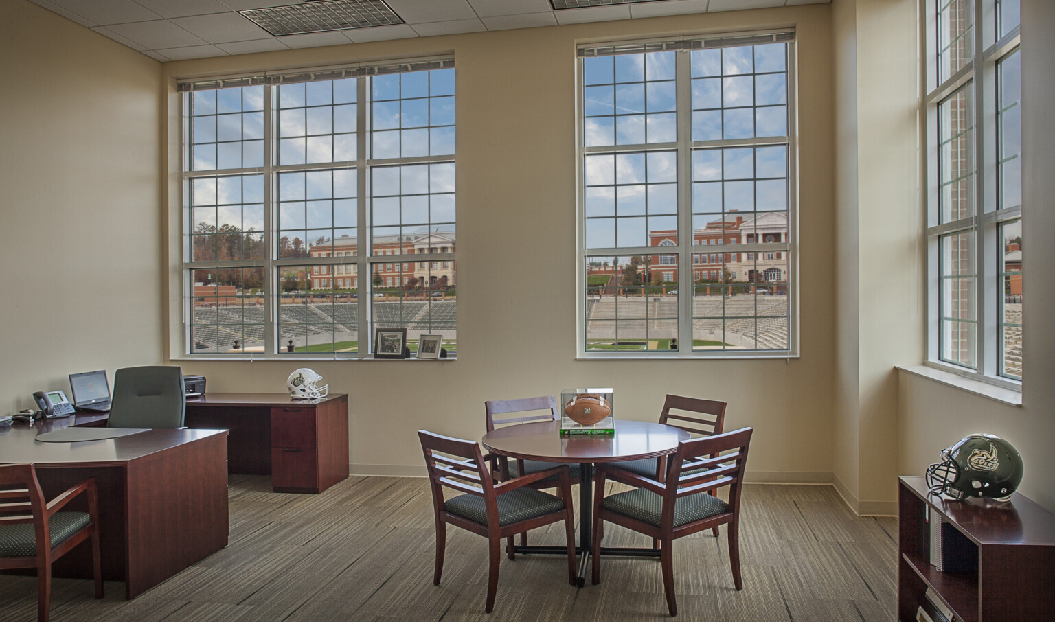 Corner office with stadium view. Horseshoe shaped wood desk in left corner with table, right, with football in display box