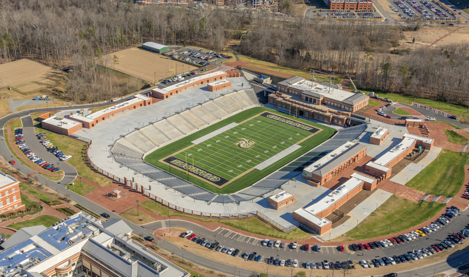 Aerial view of empty under grade level horseshoe shaped football stadium. Multistory brick building at far end of field