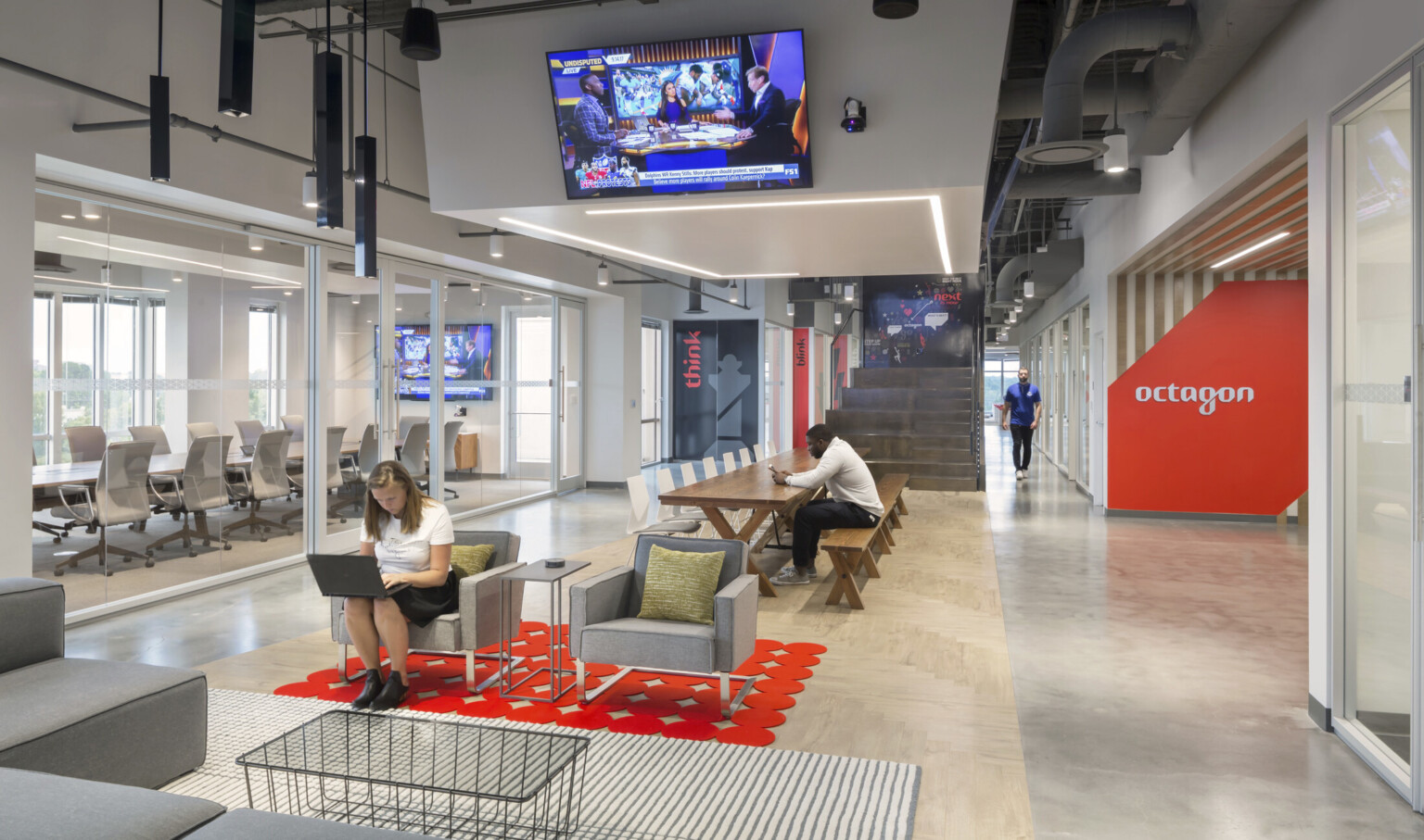 central red carpet, glass wall meeting area to left with office space, and red branding for Octagon, right, on striped wall central red carpet, glass wall meeting area to left with office space, and red branding for Octagon, right, on striped wall