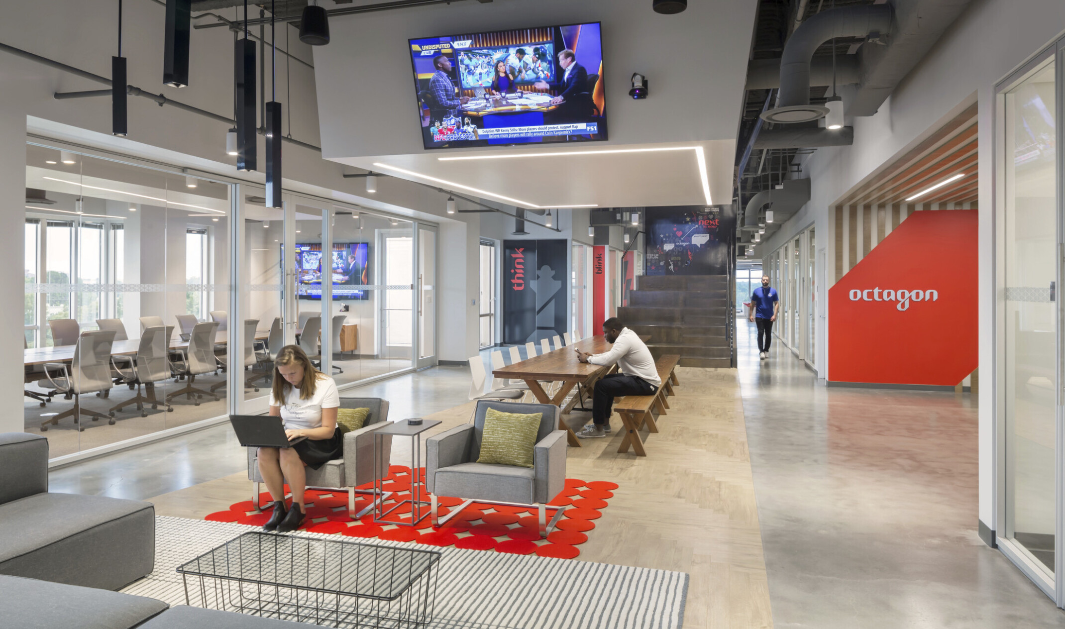 central red carpet, glass wall meeting area to left with office space, and red branding for Octagon, right, on striped wall