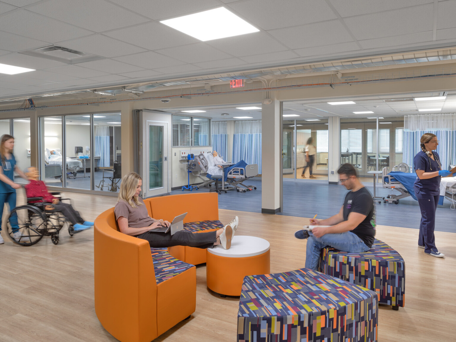 Healthcare education center showing students on modern furniture surrounded by classrooms staged as hospital rooms