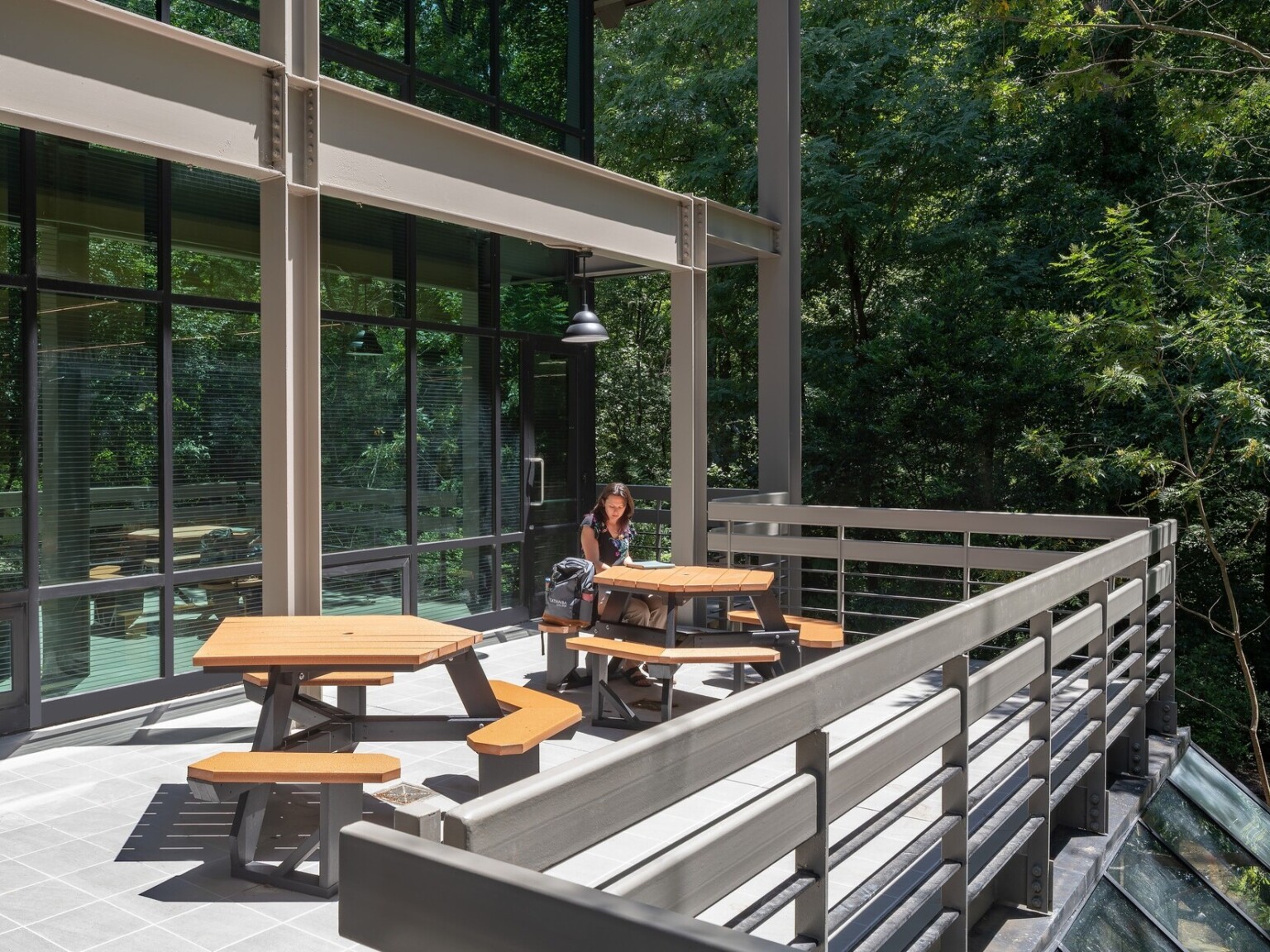 Glass building windows with brown beams and railings with picnic tables surrounded by nature