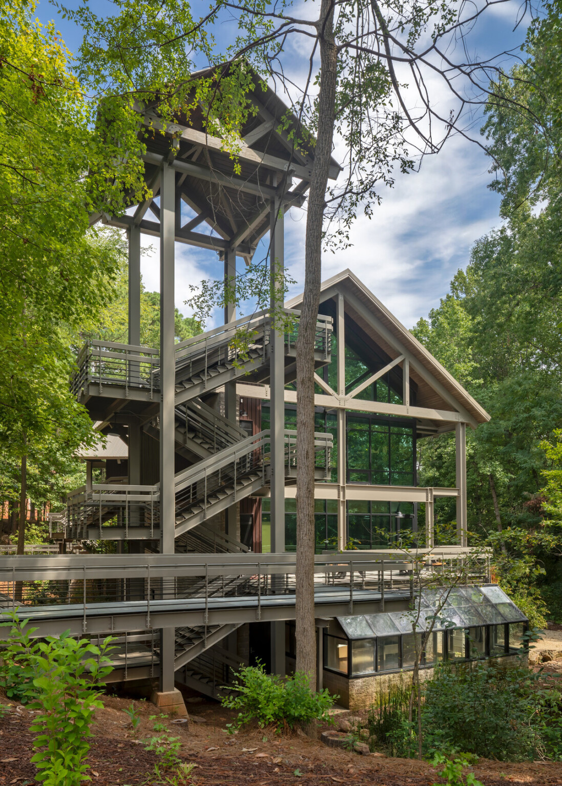 Glass facade multi story academic building with mass timber wood beam accents, wood canopied stair tower and bridge surrounded by nature