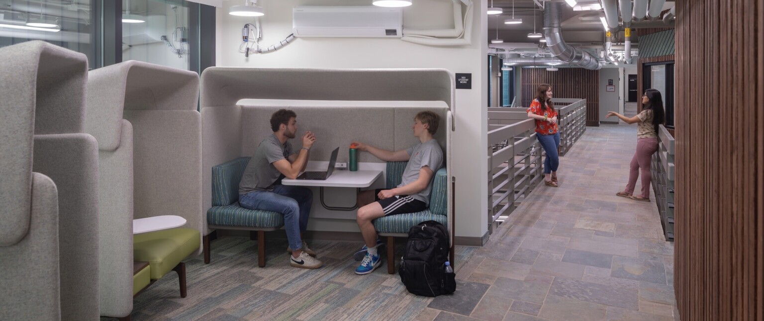 Flexible canopy enclosing booth seating study space in white room off hallway, exposed pipes and ducts