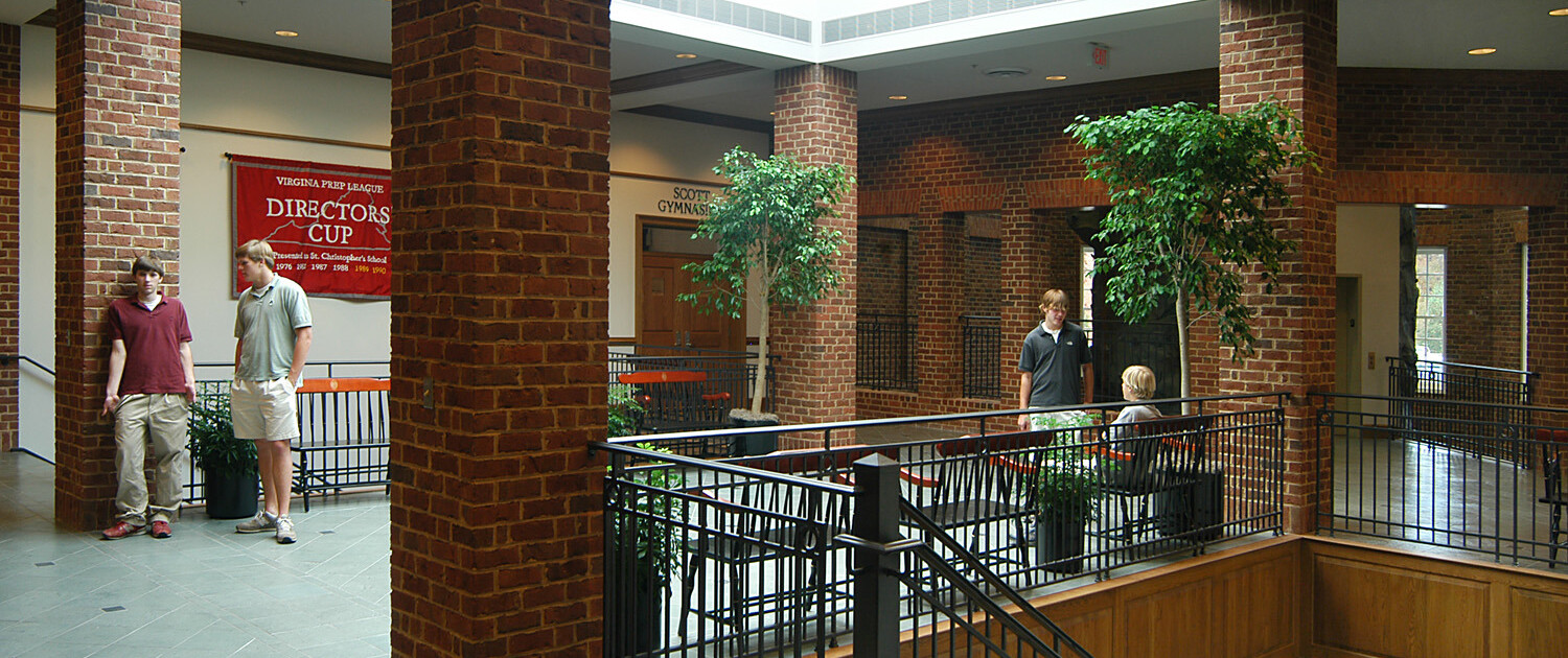 Gathering space at the top of a stairway surrounded by brick columns and a large skylight in the ceiling