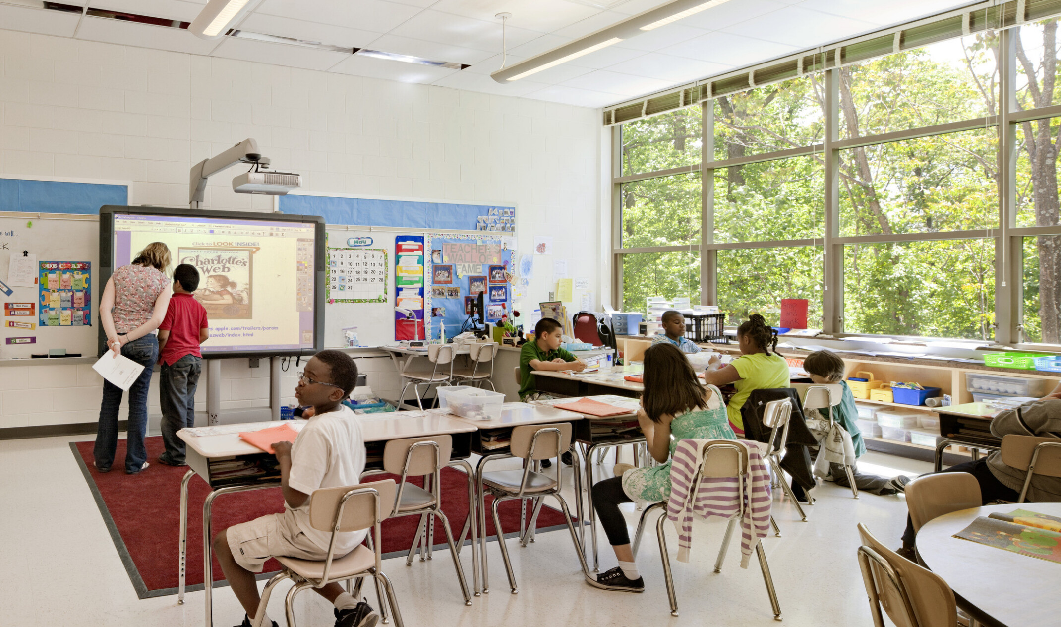 interior image of a brightly lit classroom with children at modular desks facing a background tech board