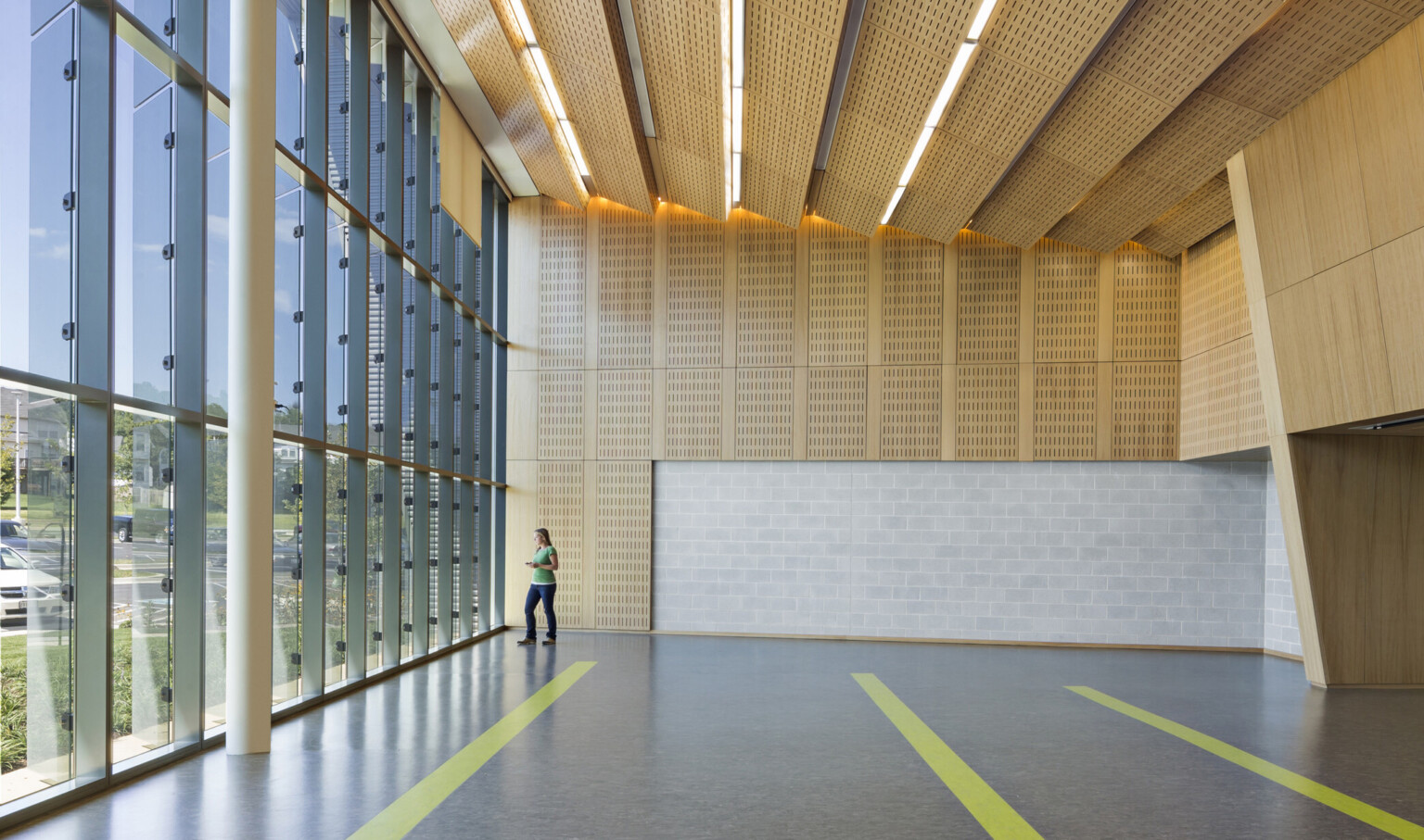 Modern interior with large glass windows, wooden ceiling and wall panels, and a person near the windows