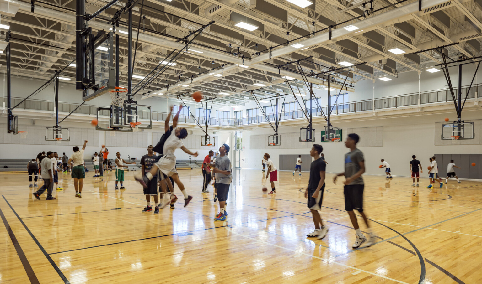 An indoor gymnasium filled with people playing basketball at multiple goals throughout the gym