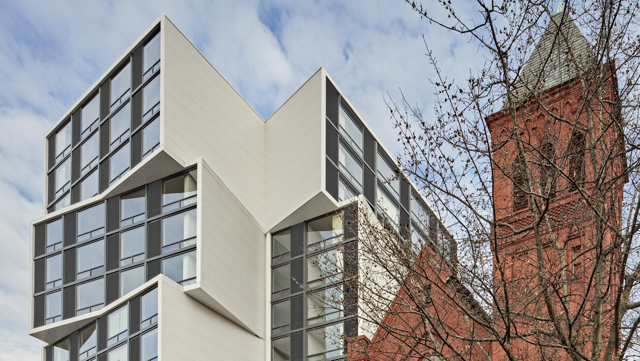 Modern building with cube shaped towers stacked opposite ways with smoked glass windows between two red brick buildings