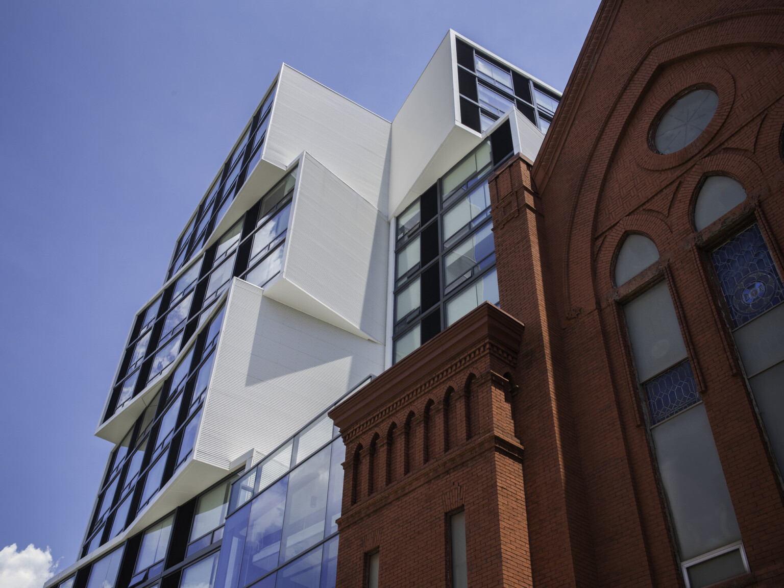 A white modern building with stacked squares filled with windows overlooking a red brick building