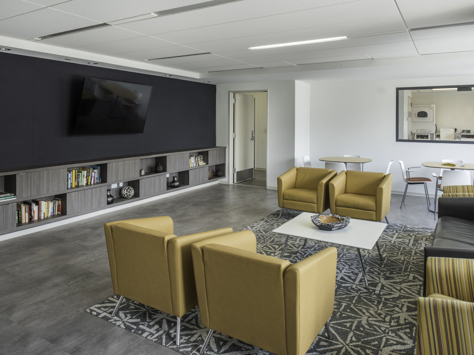 Modern yellow chairs in a lounge with a tv hanging on a black wall with grey cabinetry