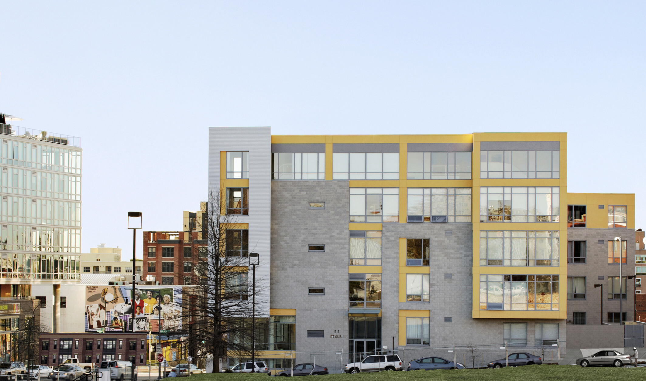 exterior facade image of a multi-shaped building; gray foundations with yellow accents on the top floors