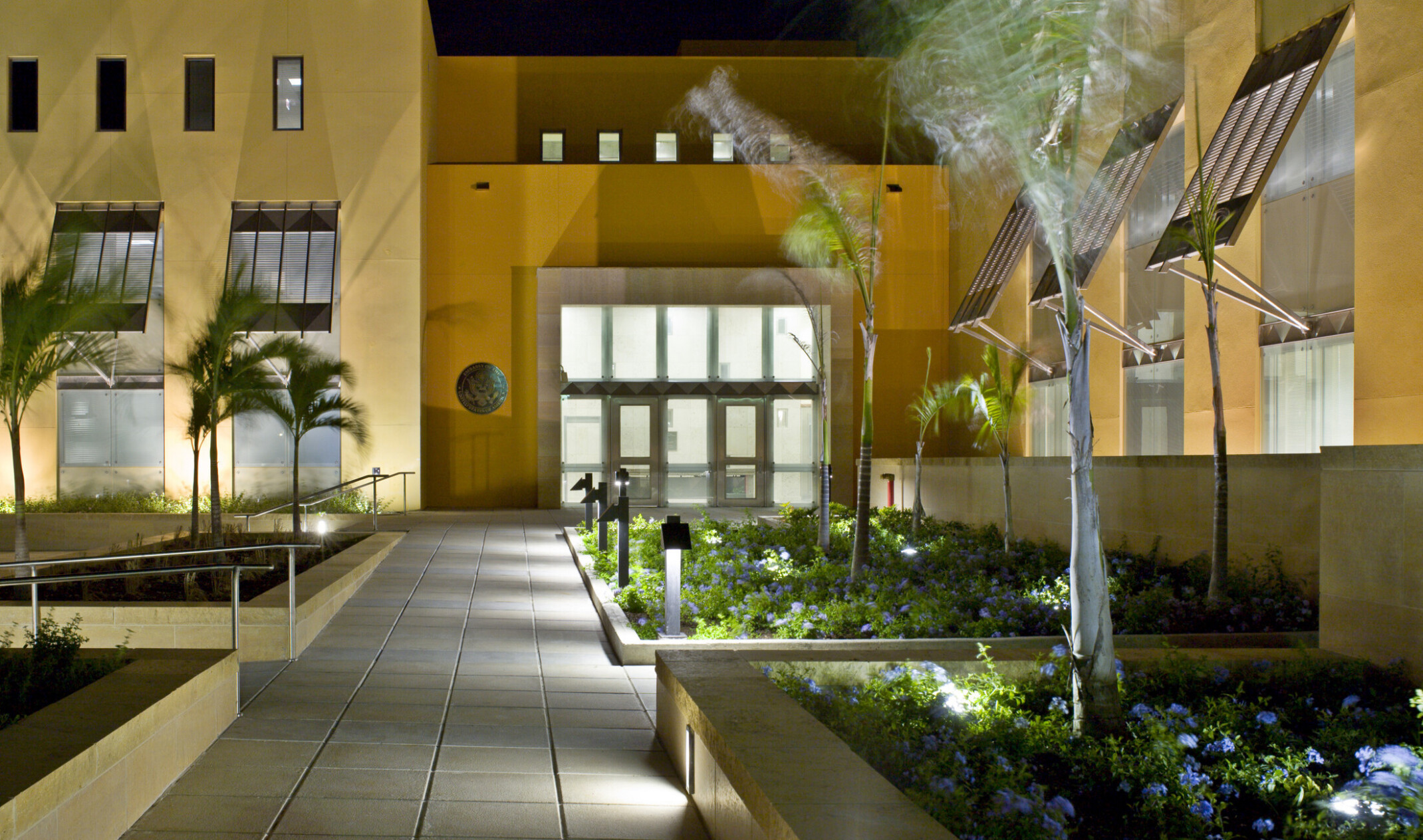 Nighttime image of the courtyard of a yellow building with walkways and planters