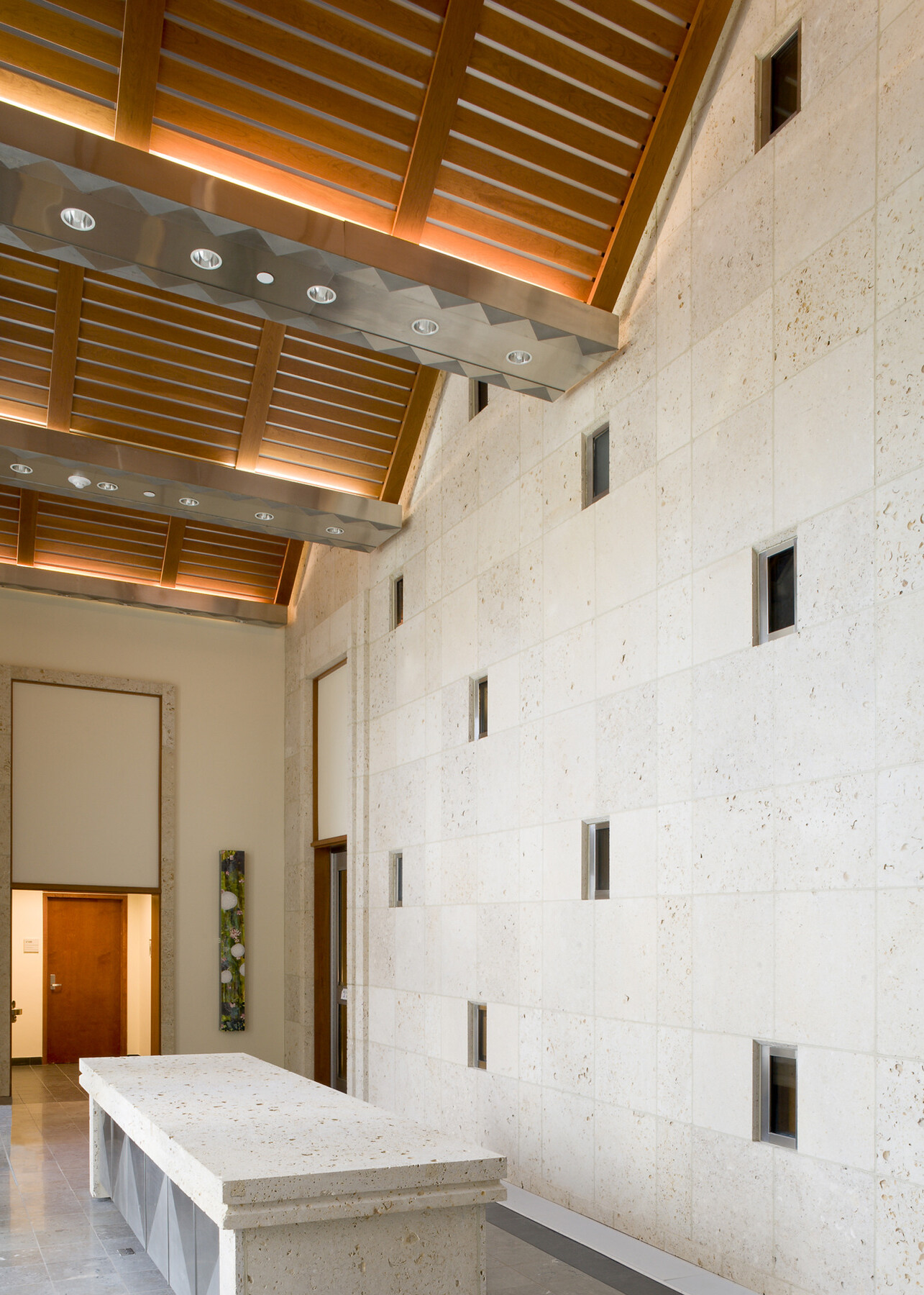 interior image of US embassy in Barbados; white stone wall with small cut outs meets a triangular wood ceiling