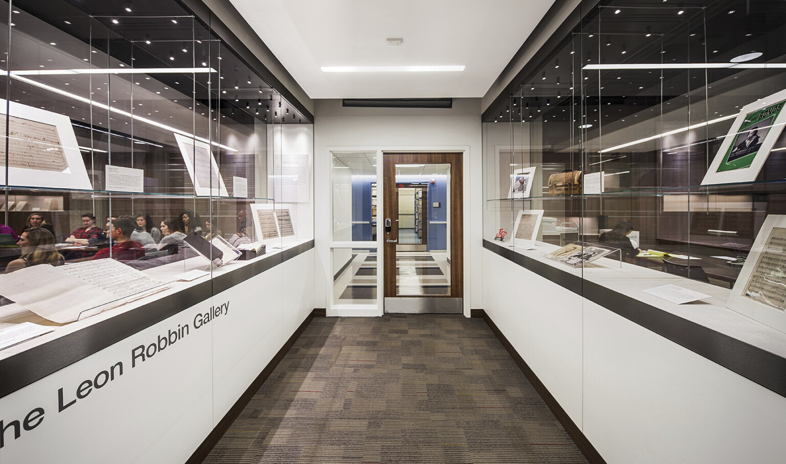 hallway of an academic library building with students seen through glass on the left and awards, plaques, and frames through glass on the right hallway of an academic library building with students seen through glass on the left and awards, plaques, and frames through glass on the right