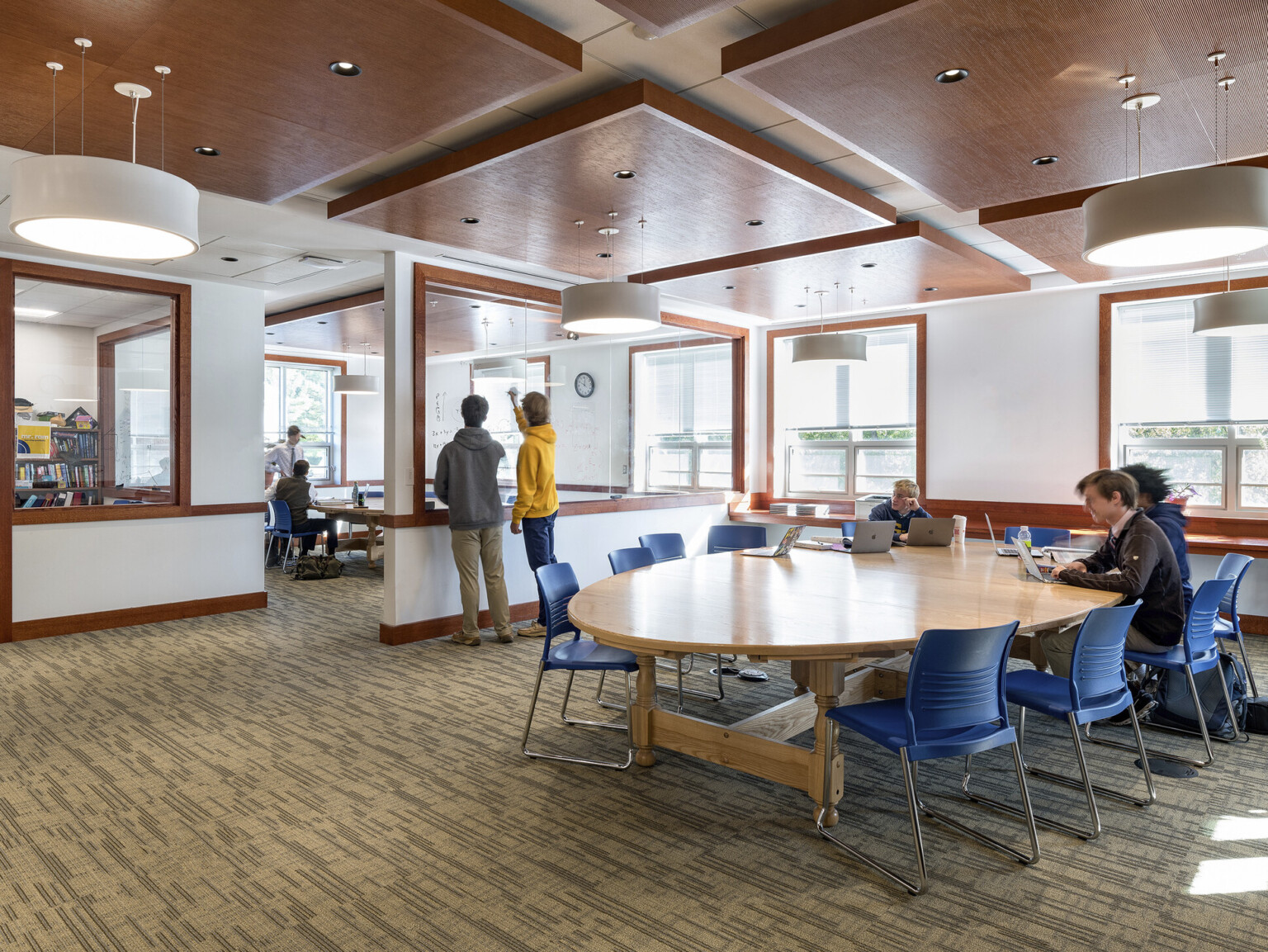 Learning center with open areas and marker boards for collaboration around rounded tables with glass windows facing exteriors.