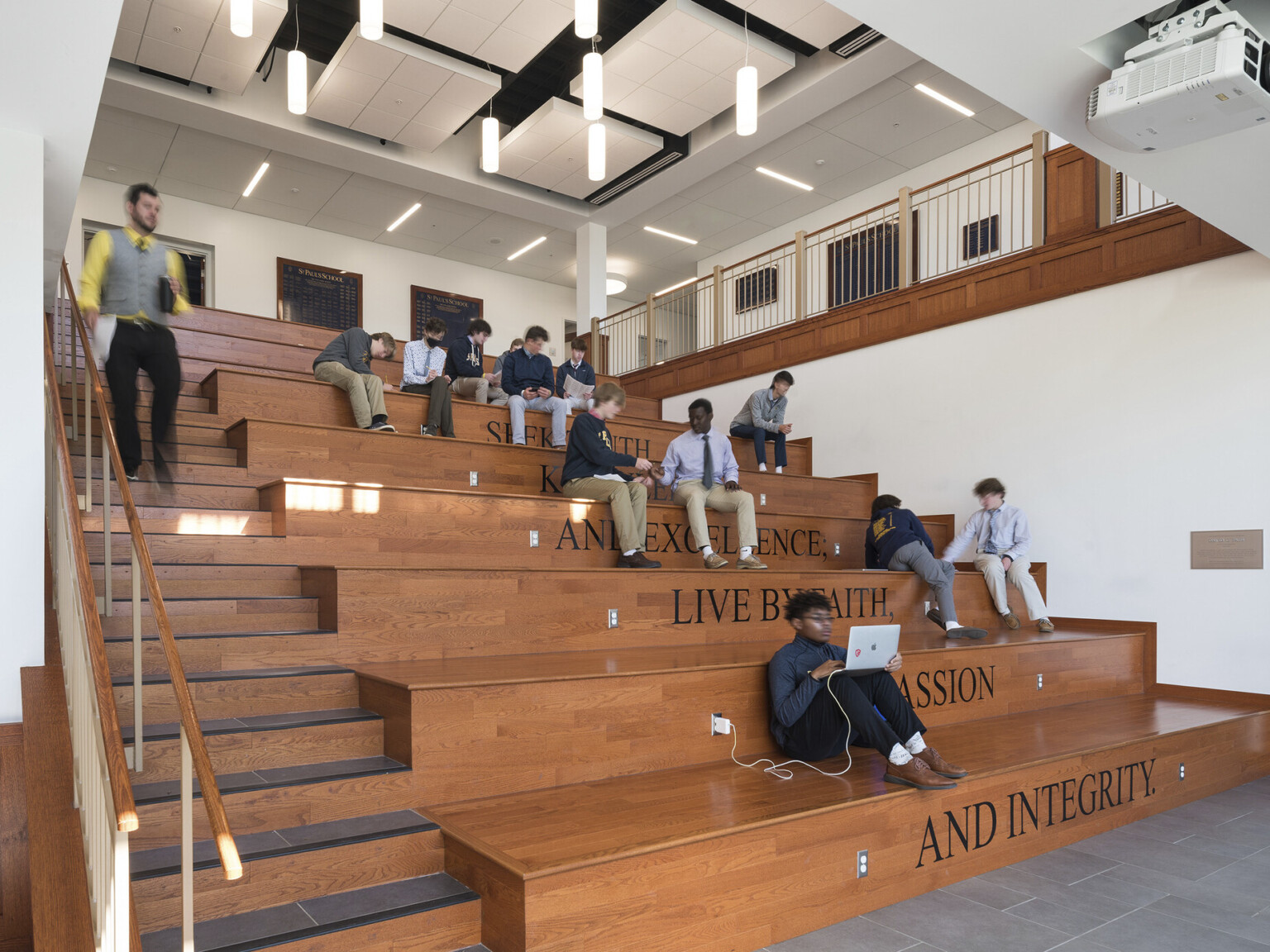 Open air learning stairs with multimedia access for collaboration, seated below pendant lights and acoustic ceiling cloud.